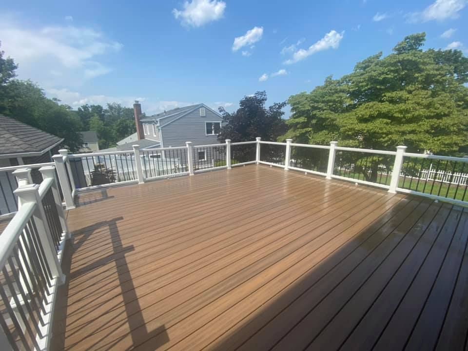 A large wooden deck with a white railing and a view of a house.