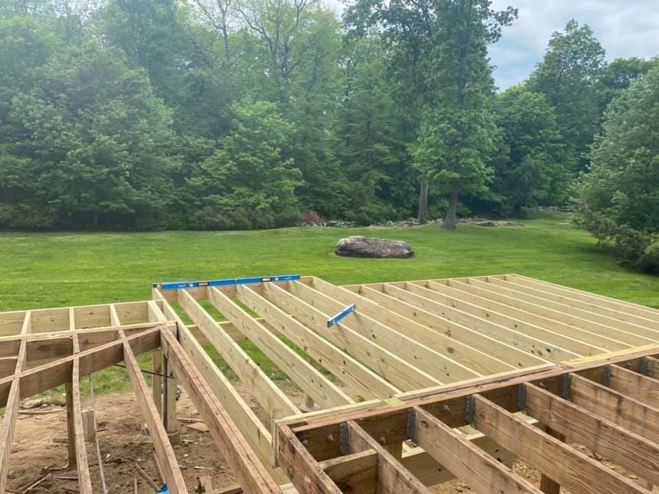 A wooden deck is being built in a backyard with trees in the background.