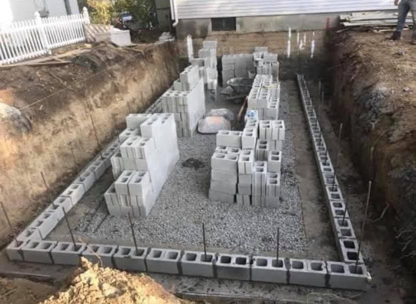 A large pile of concrete blocks is sitting in a trench next to a house.