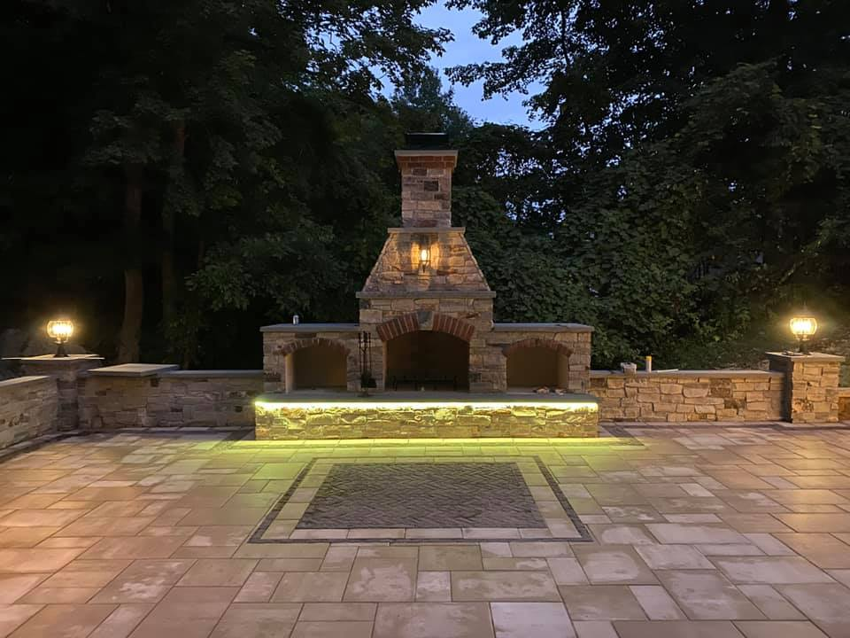 A stone fireplace is lit up at night on a patio.