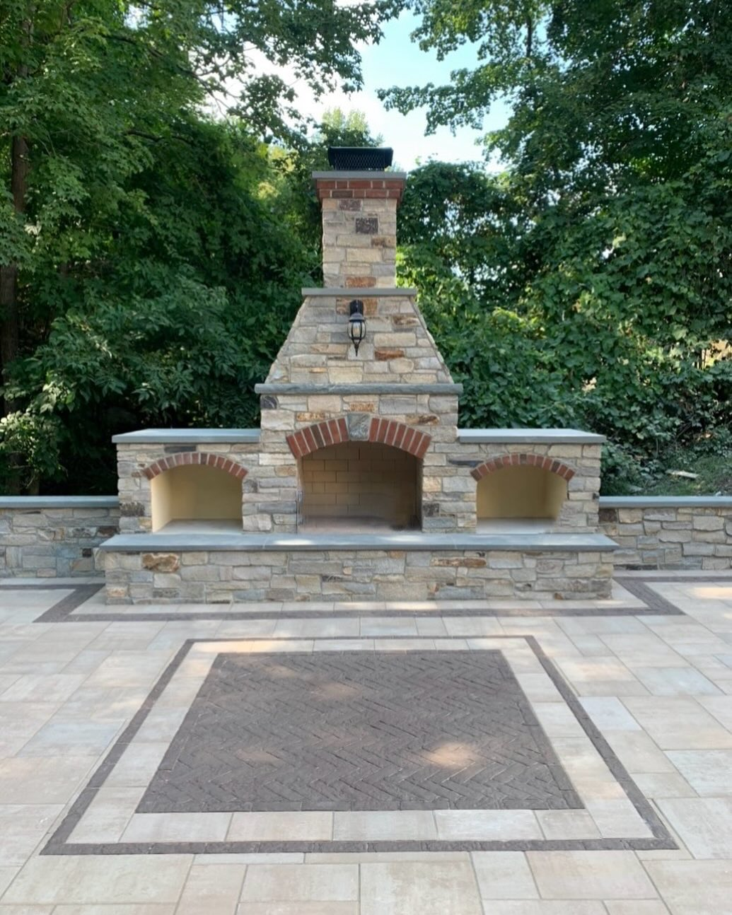 A stone fireplace is surrounded by trees on a patio