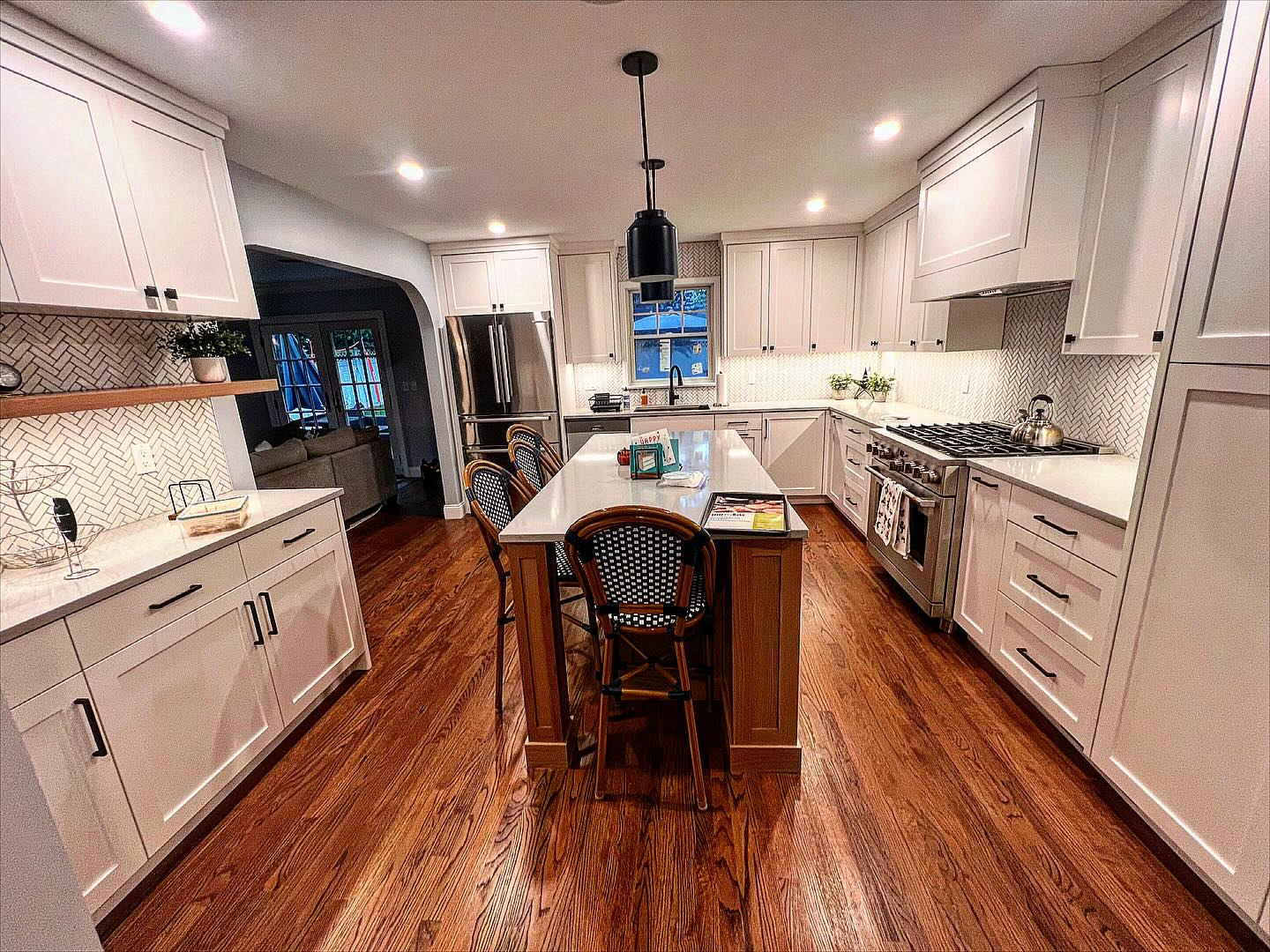 A kitchen with white cabinets and hardwood floors has a large island in the middle.
