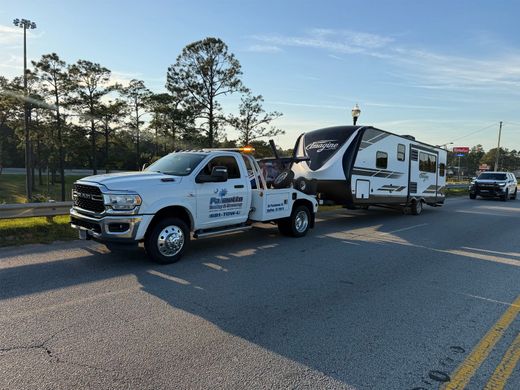 Tow truck hauling a white camper on a roadside with trees