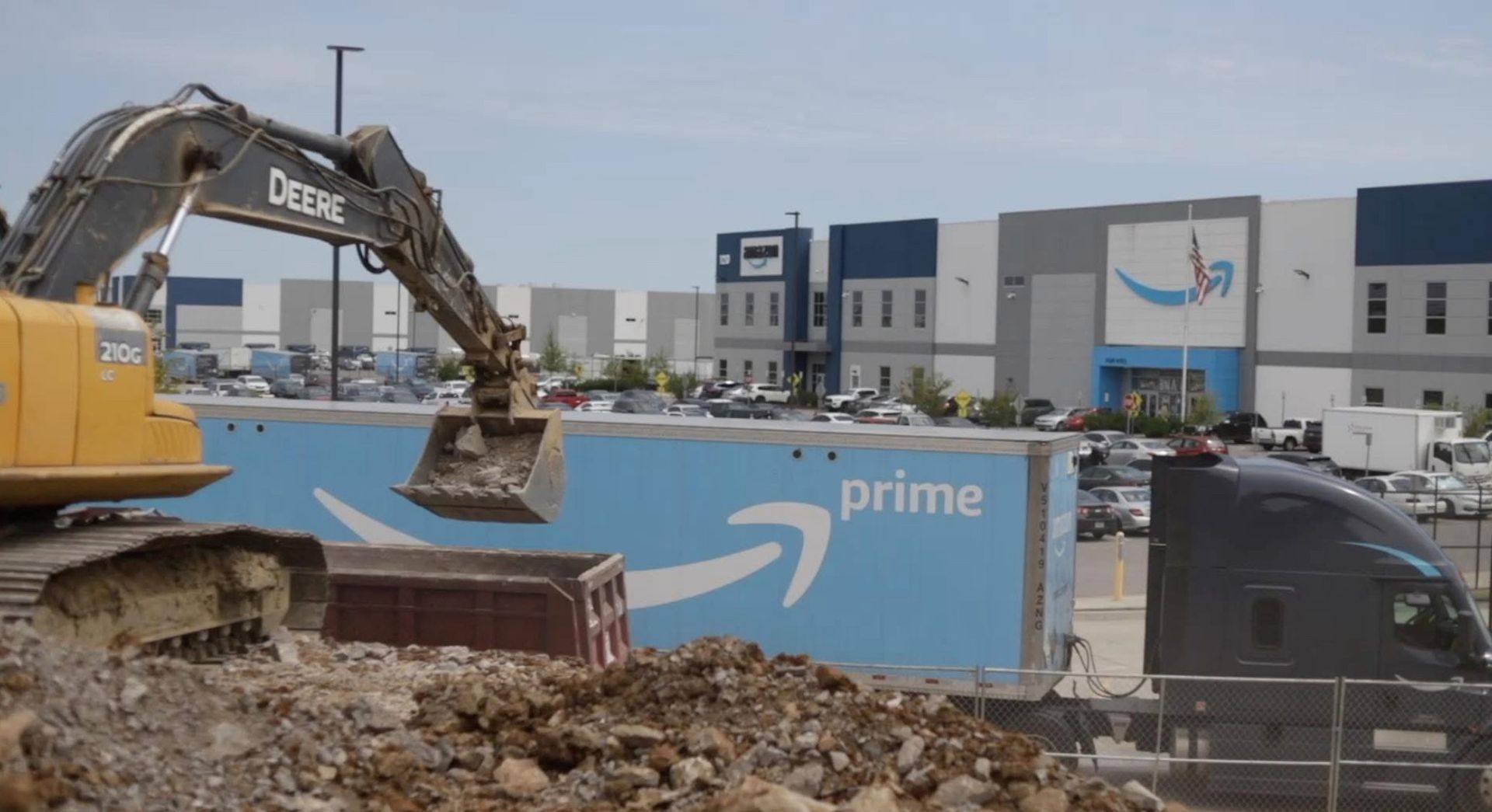 Excavator demolishing an Amazon Prime truck in front of an Amazon warehouse.