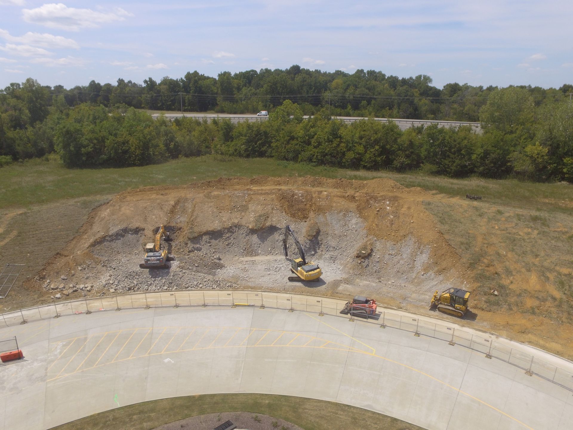 Construction site: Excavators on a hillside, removing soil next to a curved road.