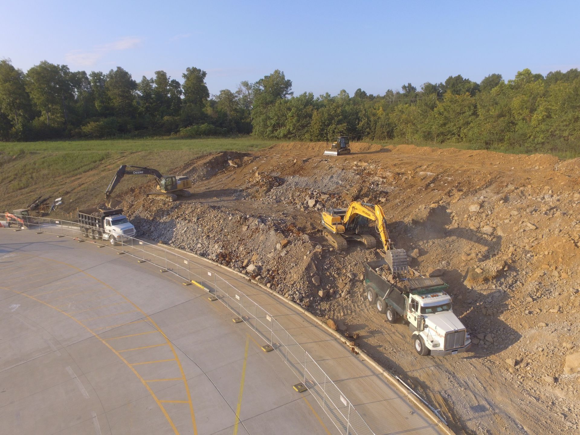 Construction site: Excavators and trucks removing debris from a roadside hillside.