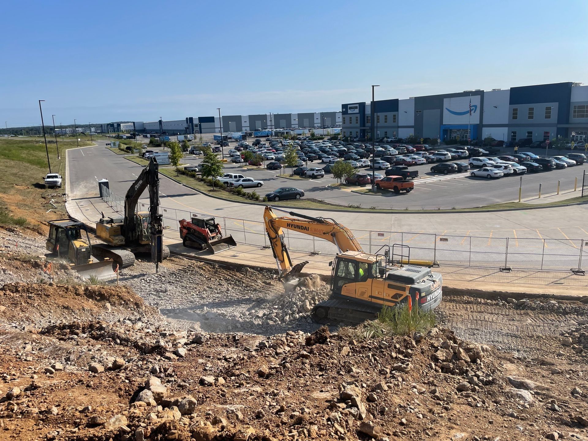 Construction site with excavators, with an Amazon warehouse in the background.