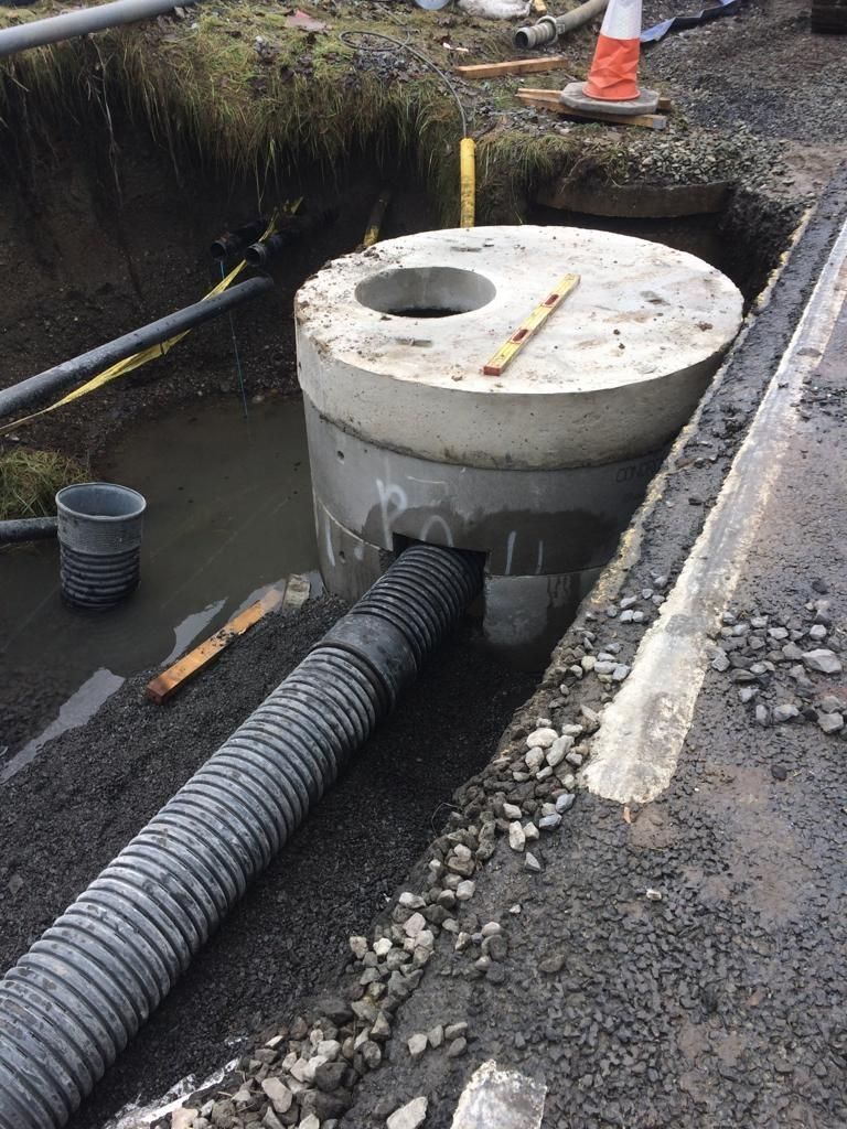 Concrete manhole in construction site ditch, with drainage pipe connected to the base.