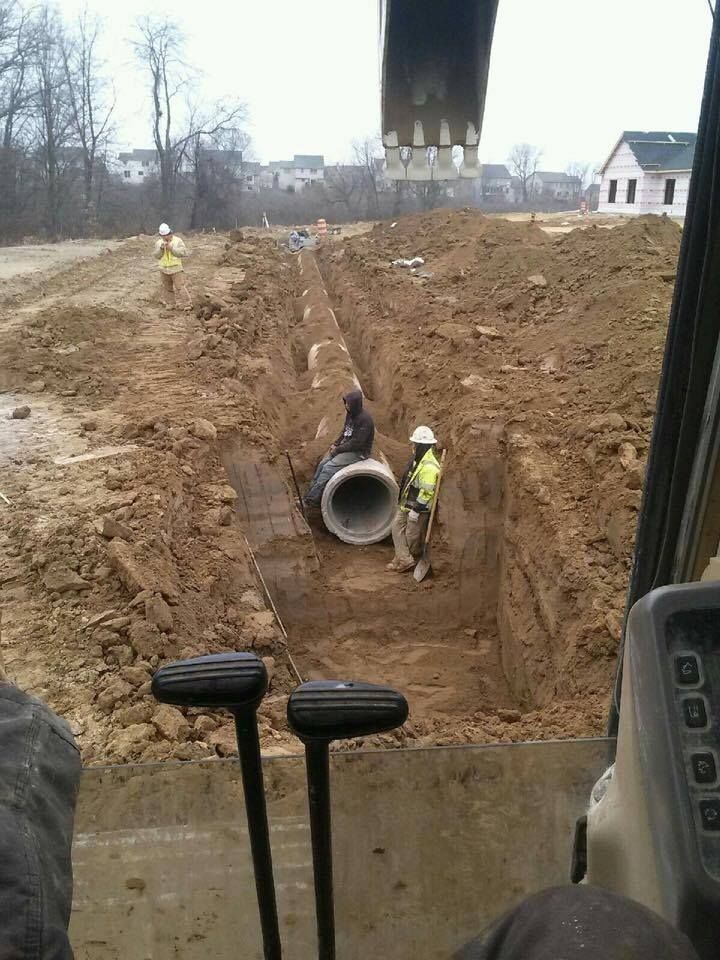 Workers installing a large pipe in a trench at a construction site.
