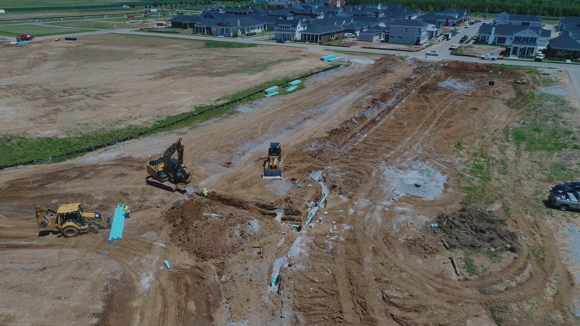 Construction site with heavy machinery moving dirt; newly built homes in background.
