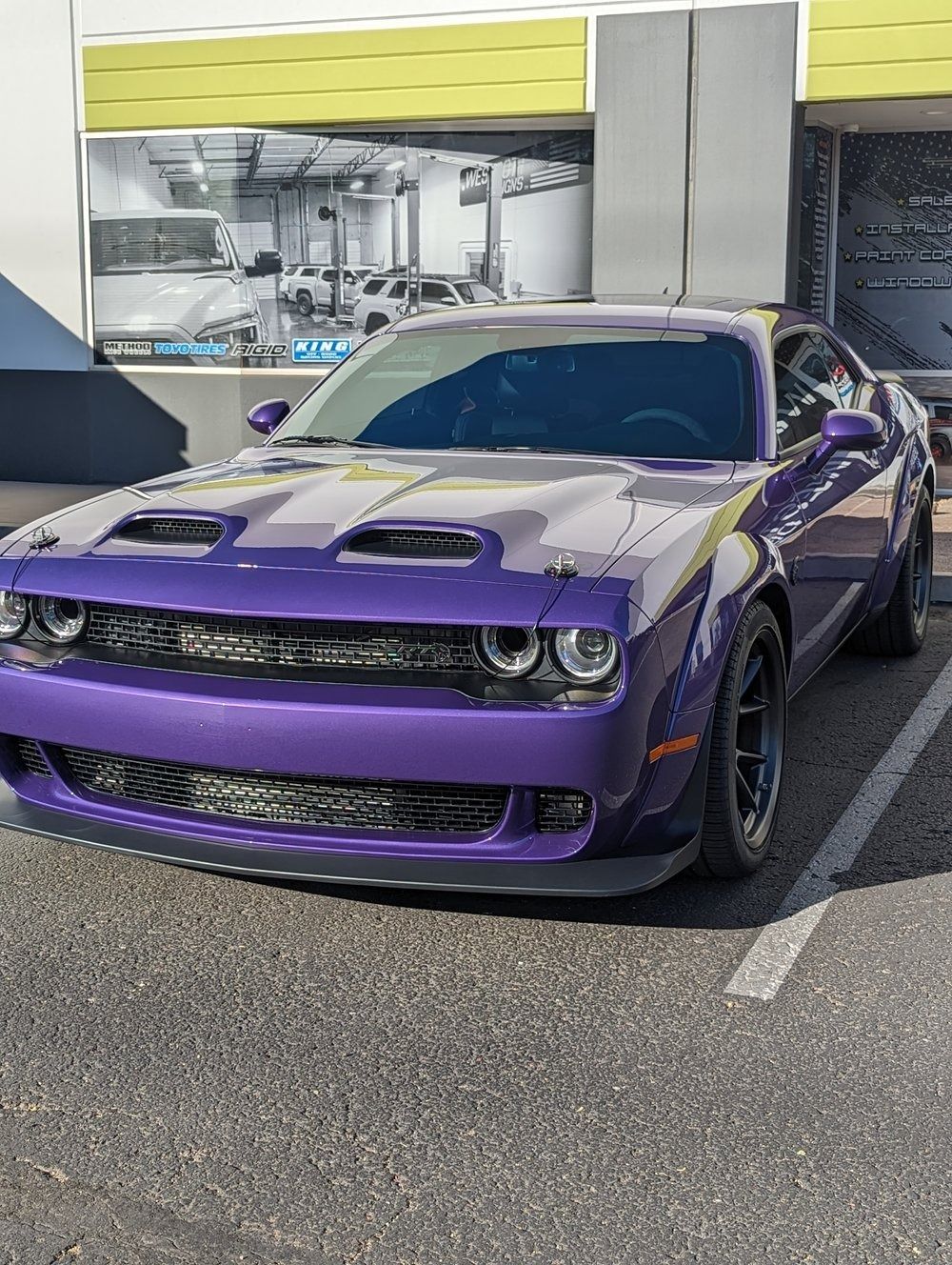 A purple dodge challenger is parked in a parking lot in front of a building.