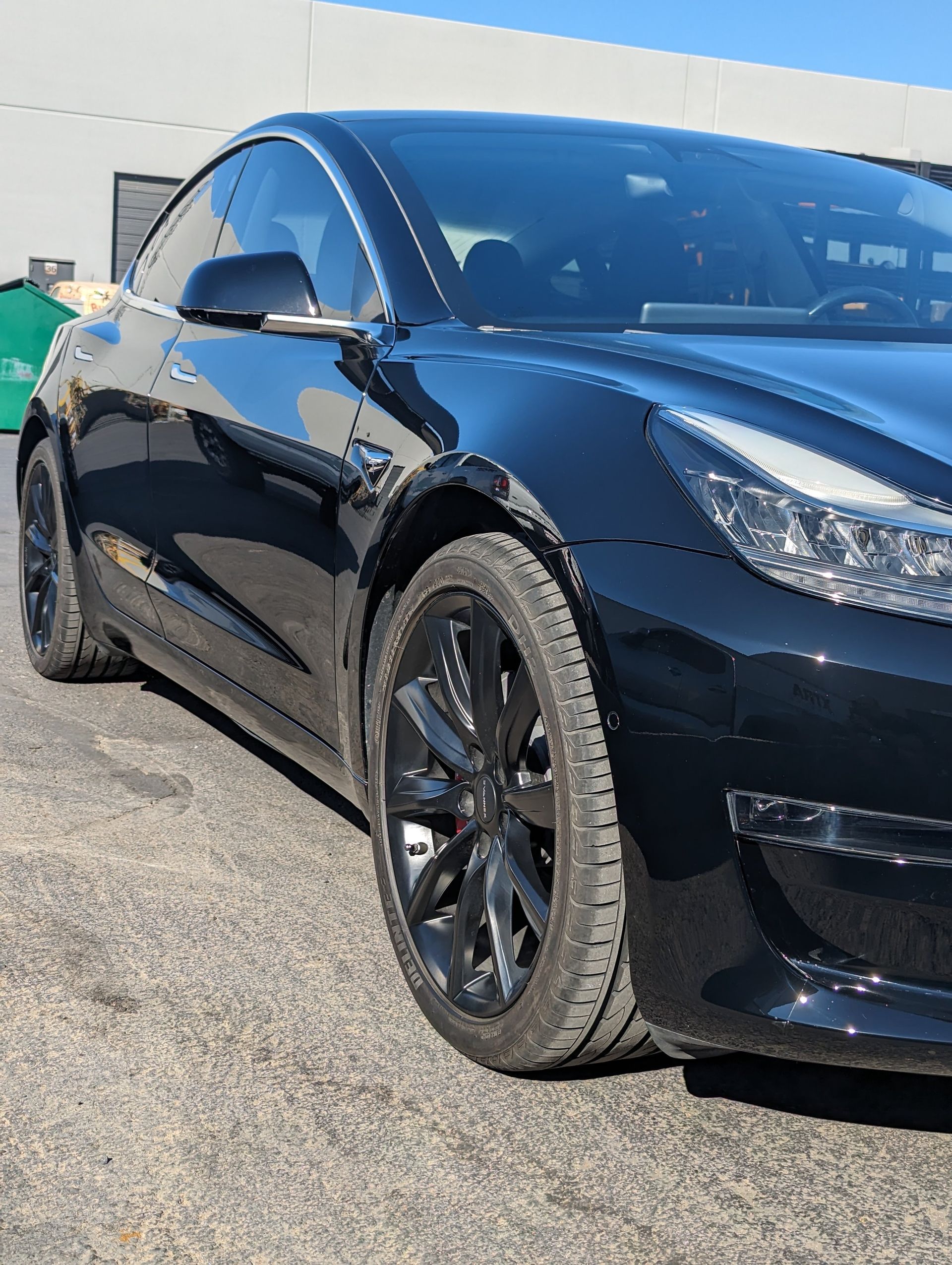 A black tesla model 3 is parked in a parking lot.