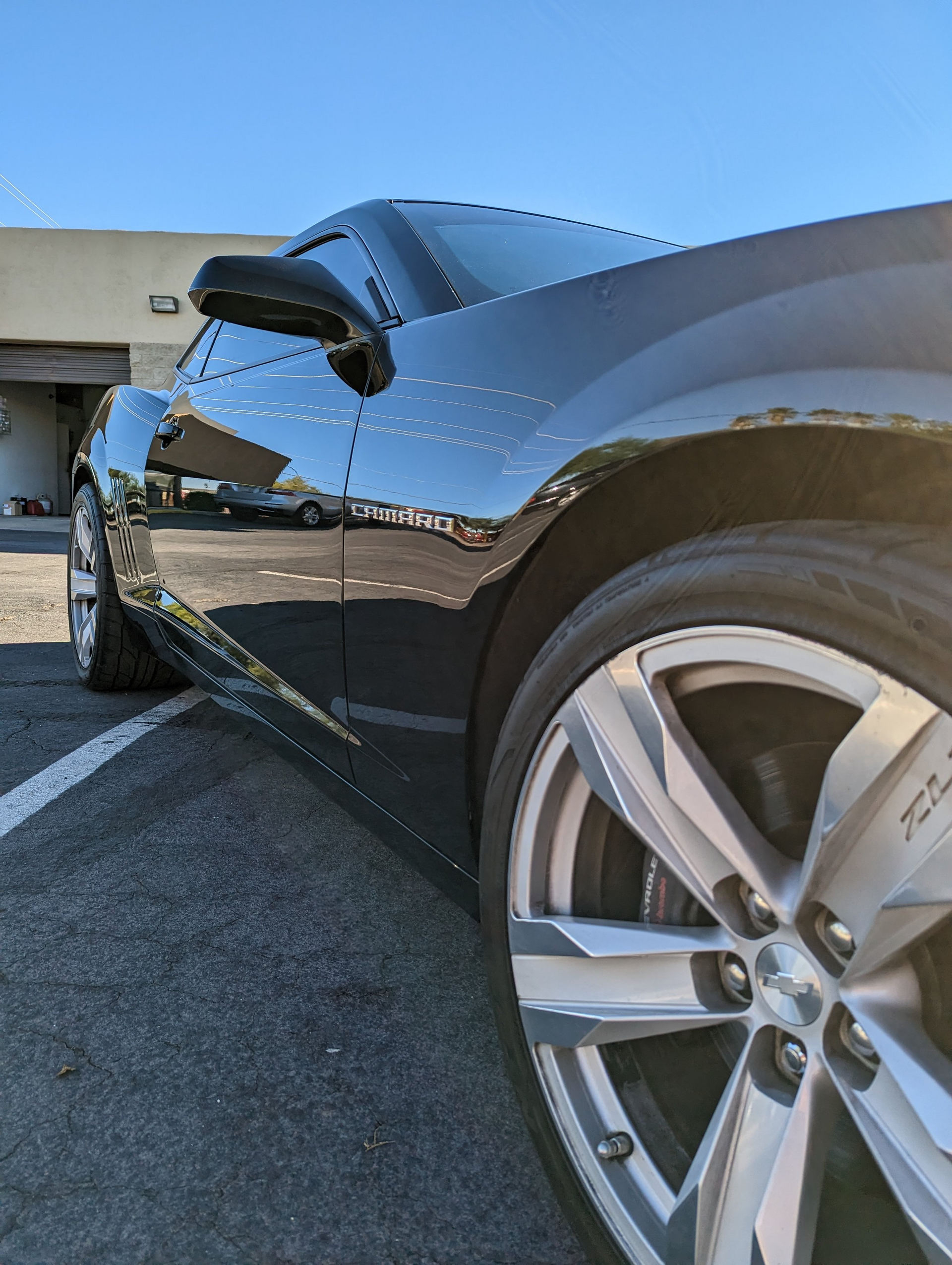 A black car is parked in a parking lot in front of a building.