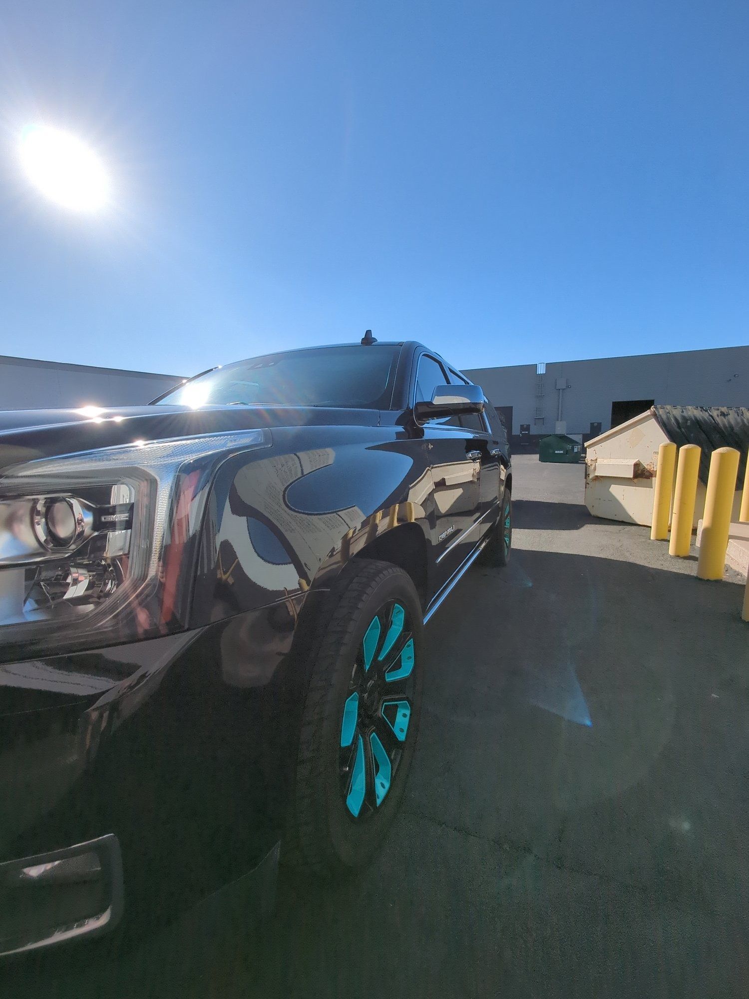 A black truck with blue wheels is parked in a parking lot.