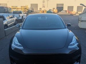A black tesla model 3 is parked in a parking lot.