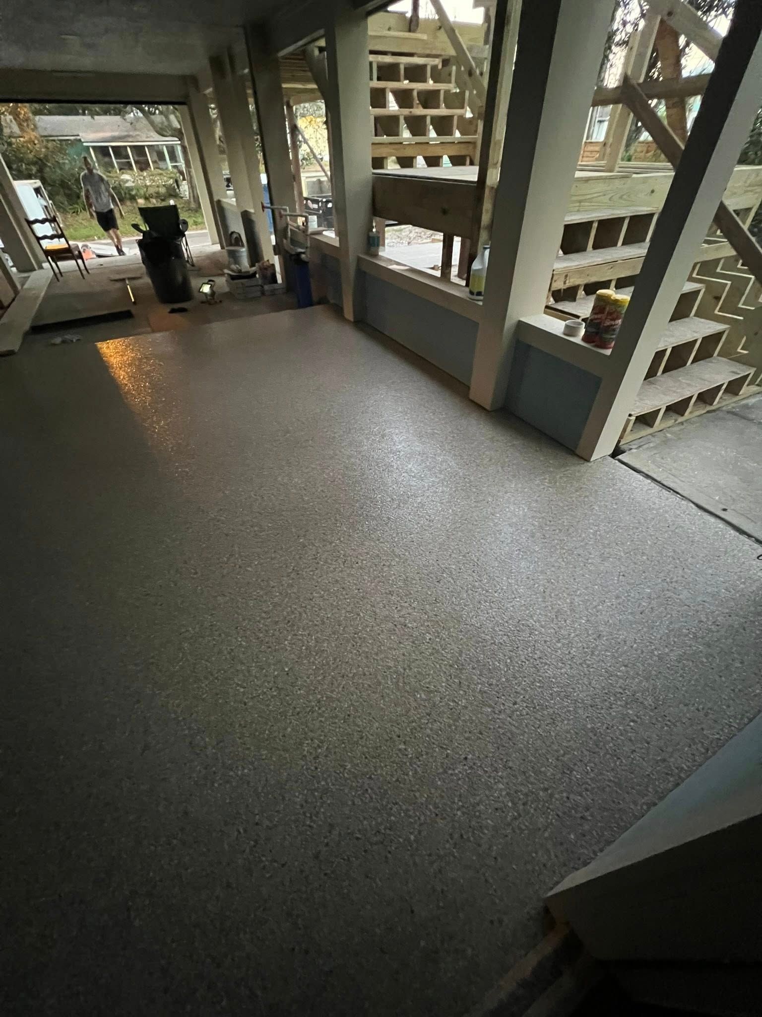A porch with a speckled gray floor, wood posts and beams, and steps leading up.