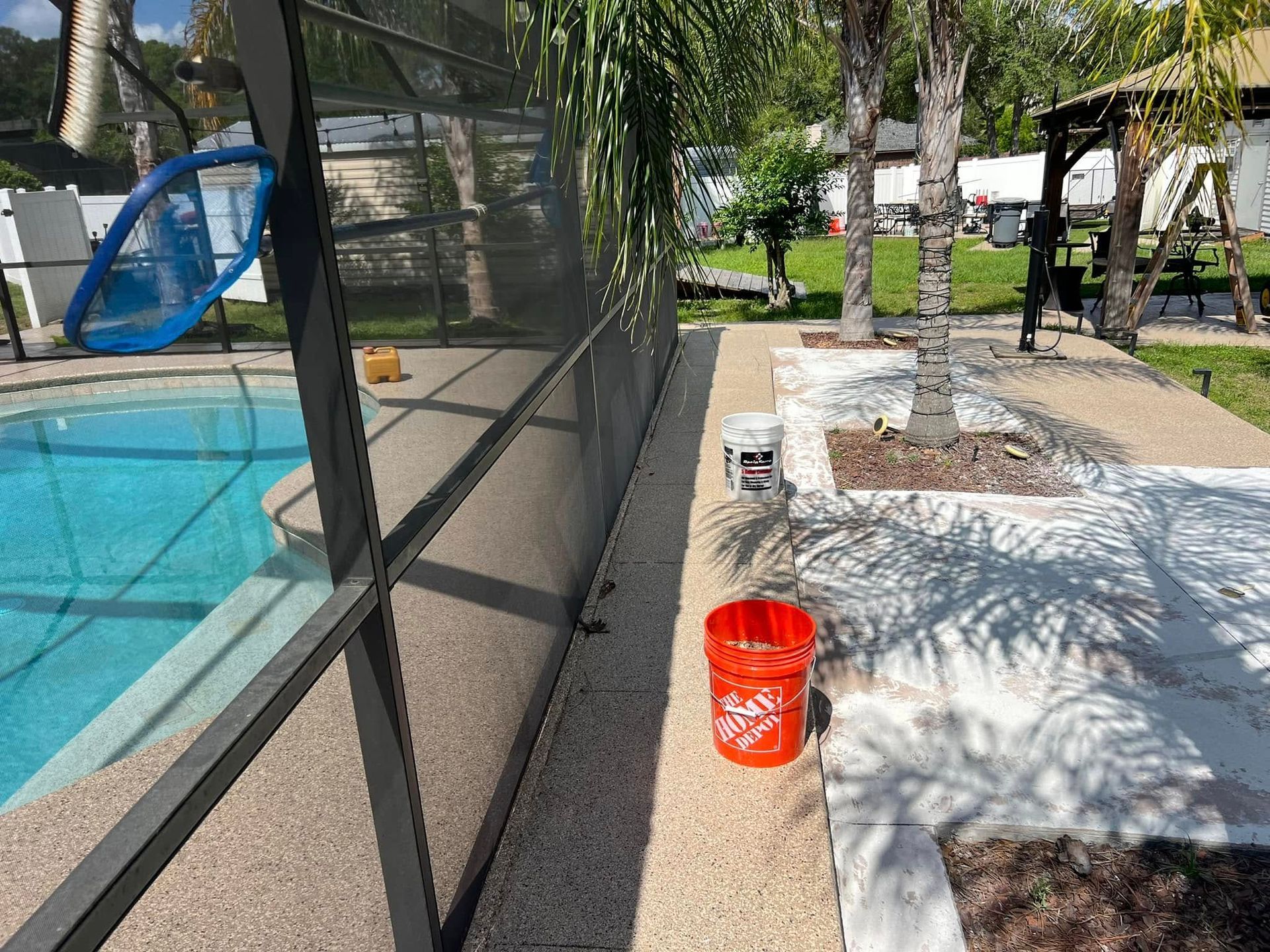 Poolside scene with a screened enclosure, cement patio, and a bright orange bucket.