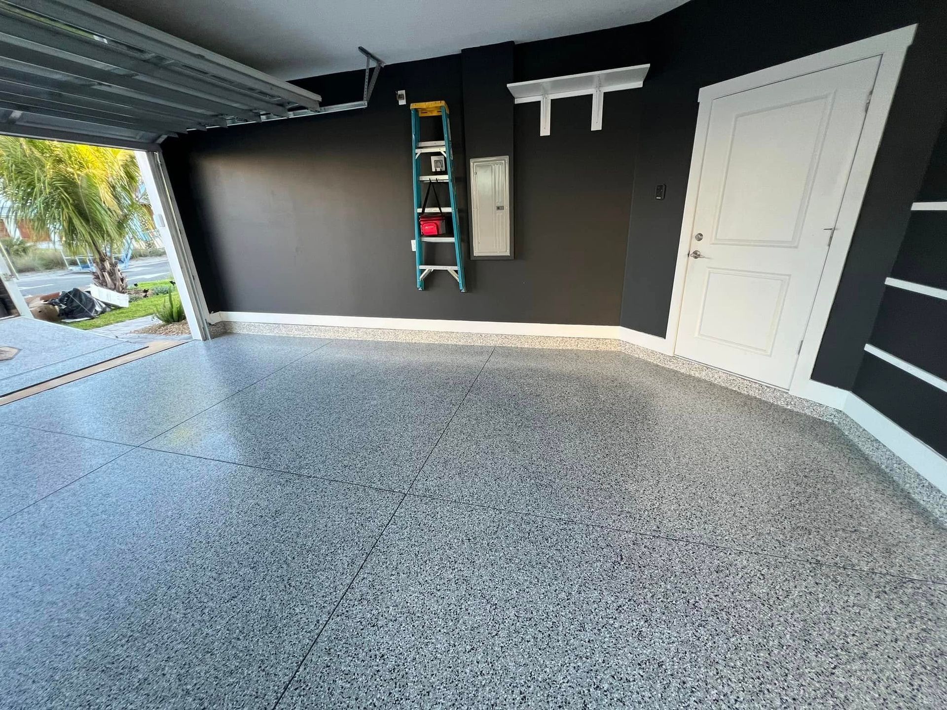 Garage with epoxy floor, black walls, white door, and a ladder.