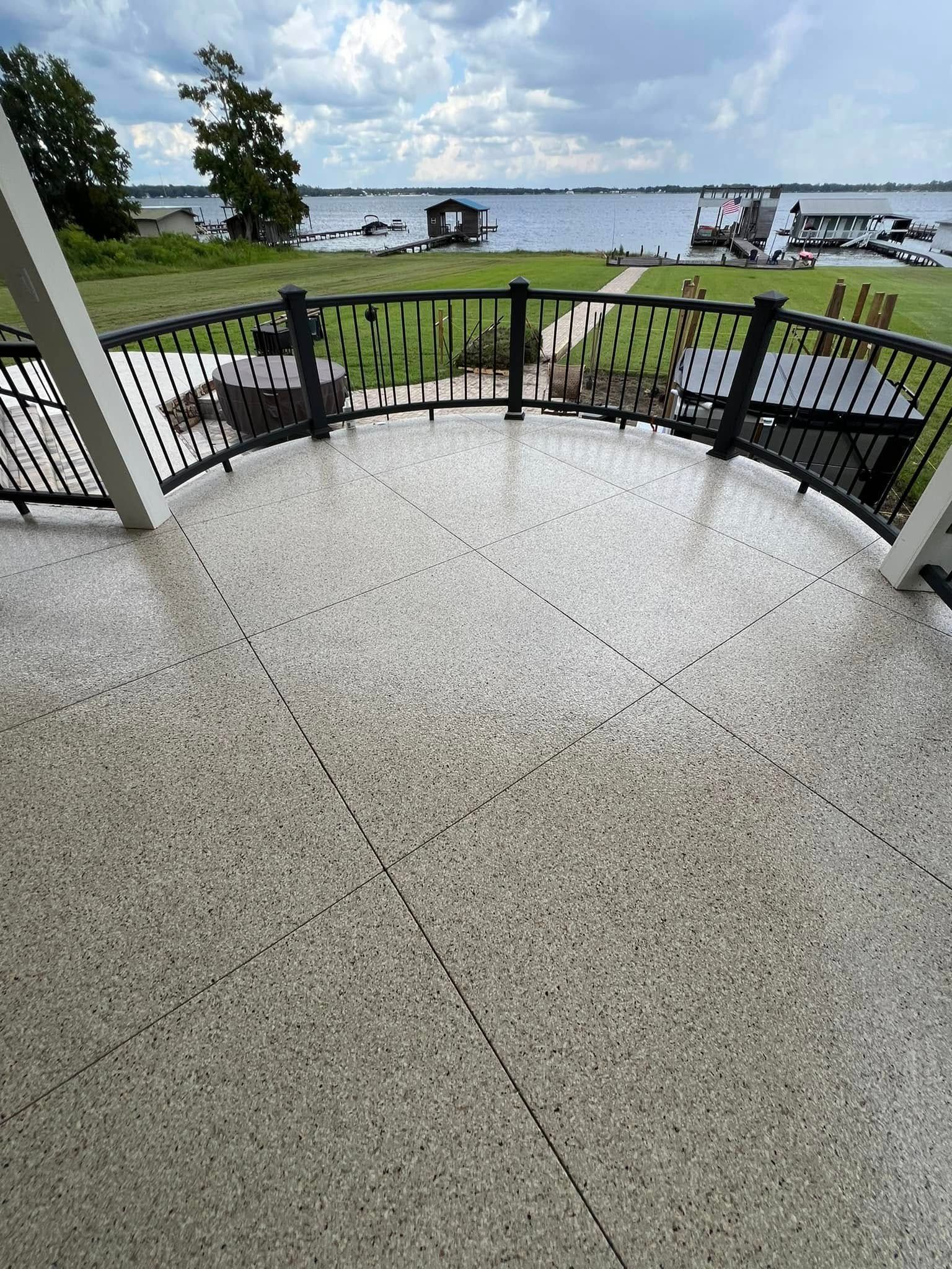 A curved, speckled patio overlooking a lake with docks, railing, and sky.