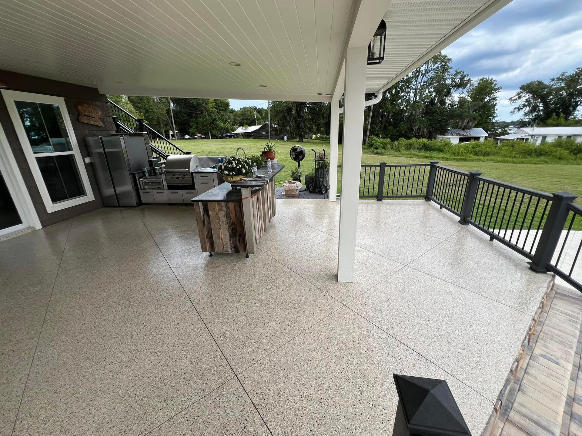 Covered outdoor kitchen and patio with gray speckled floor and black railing.