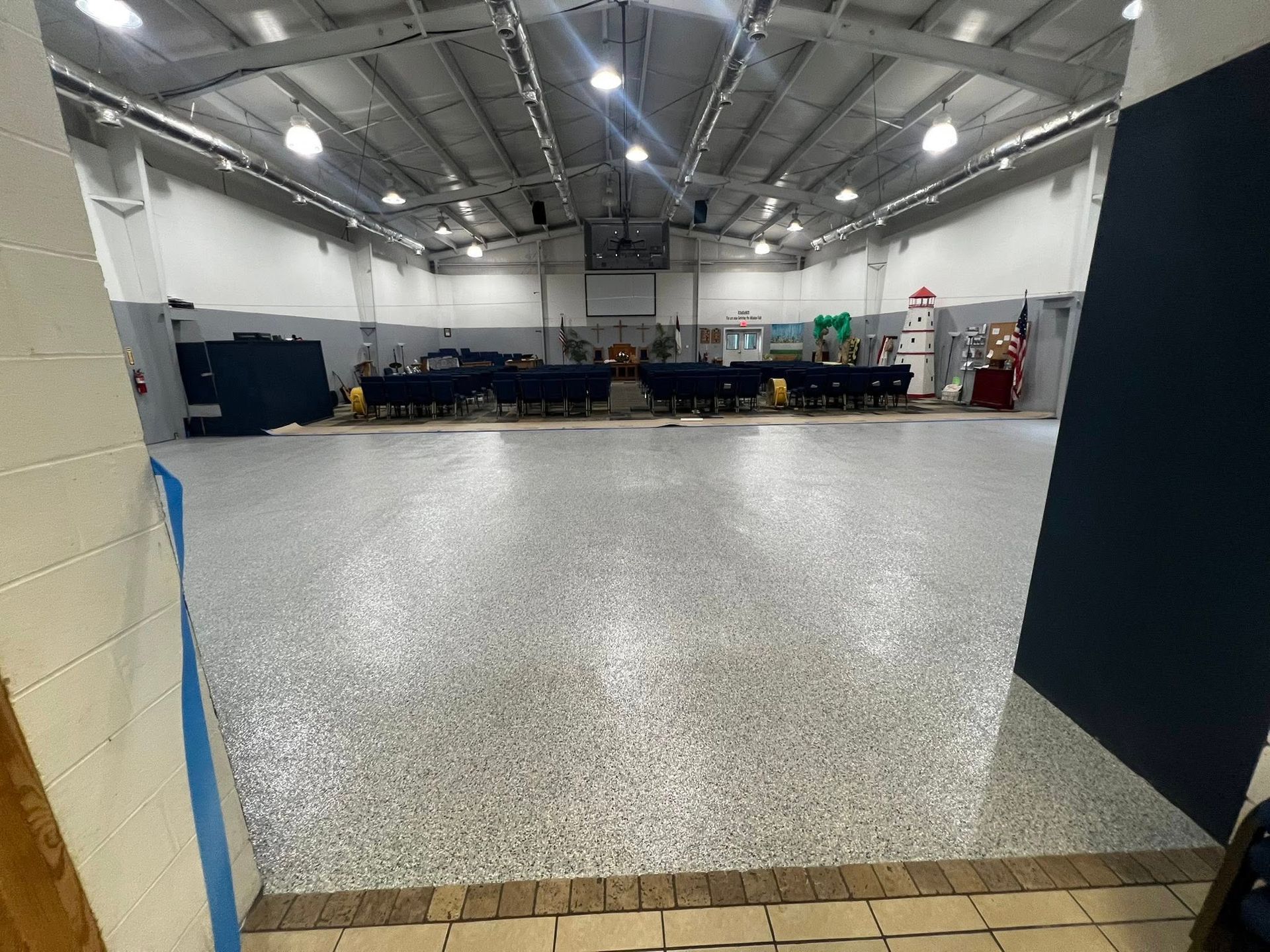 An open, empty room with a speckled gray floor, tables, and equipment against the far wall.