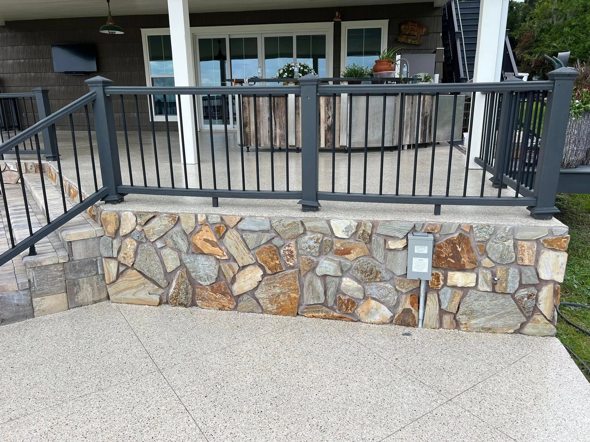 Stone wall with dark railing, concrete patio. Outdoor setting.