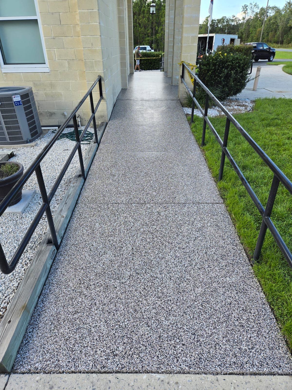 Concrete ramp with black handrails, leading to building entrance.