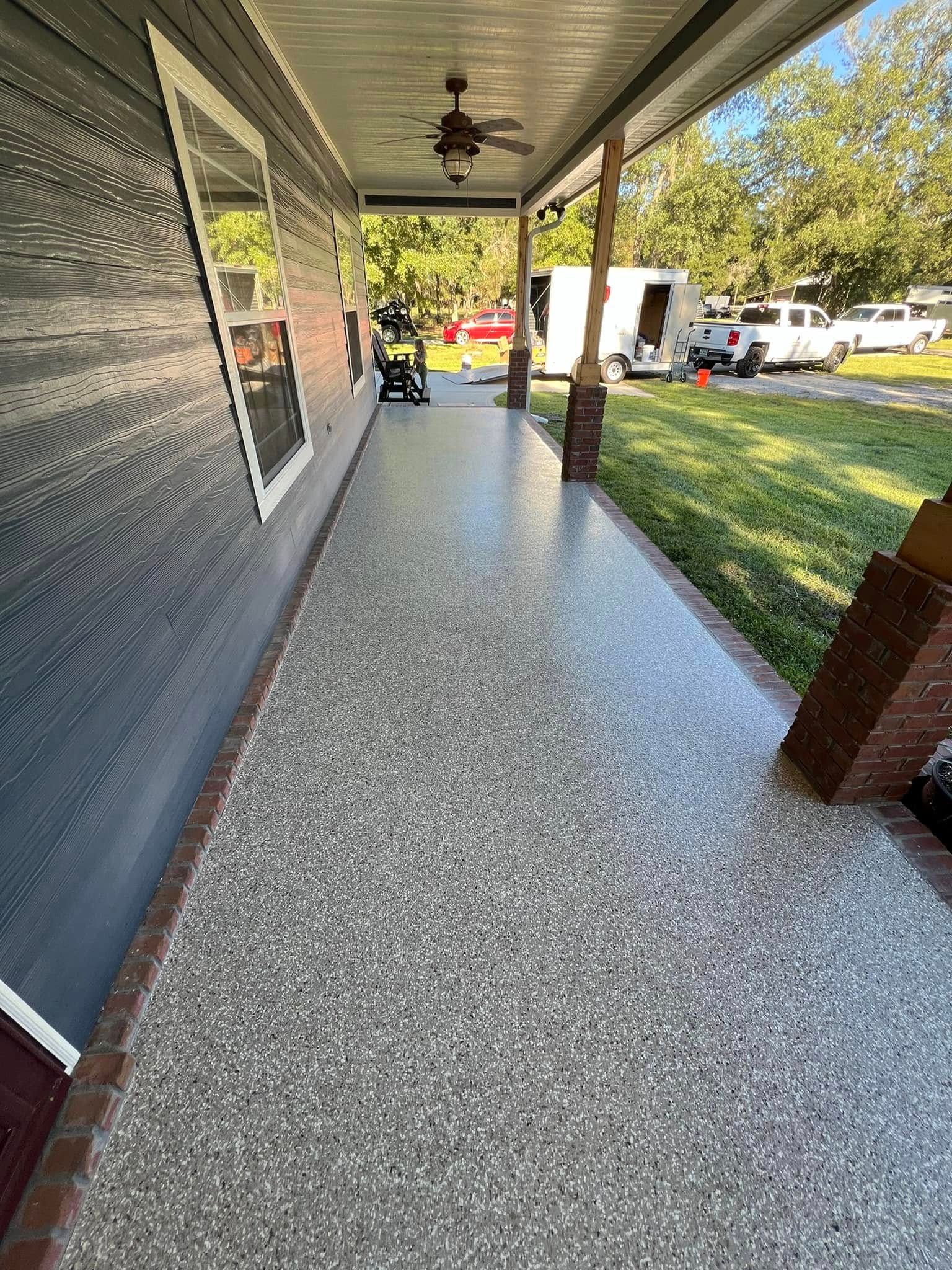 Gray speckled porch flooring with a brick border, next to a blue home exterior.