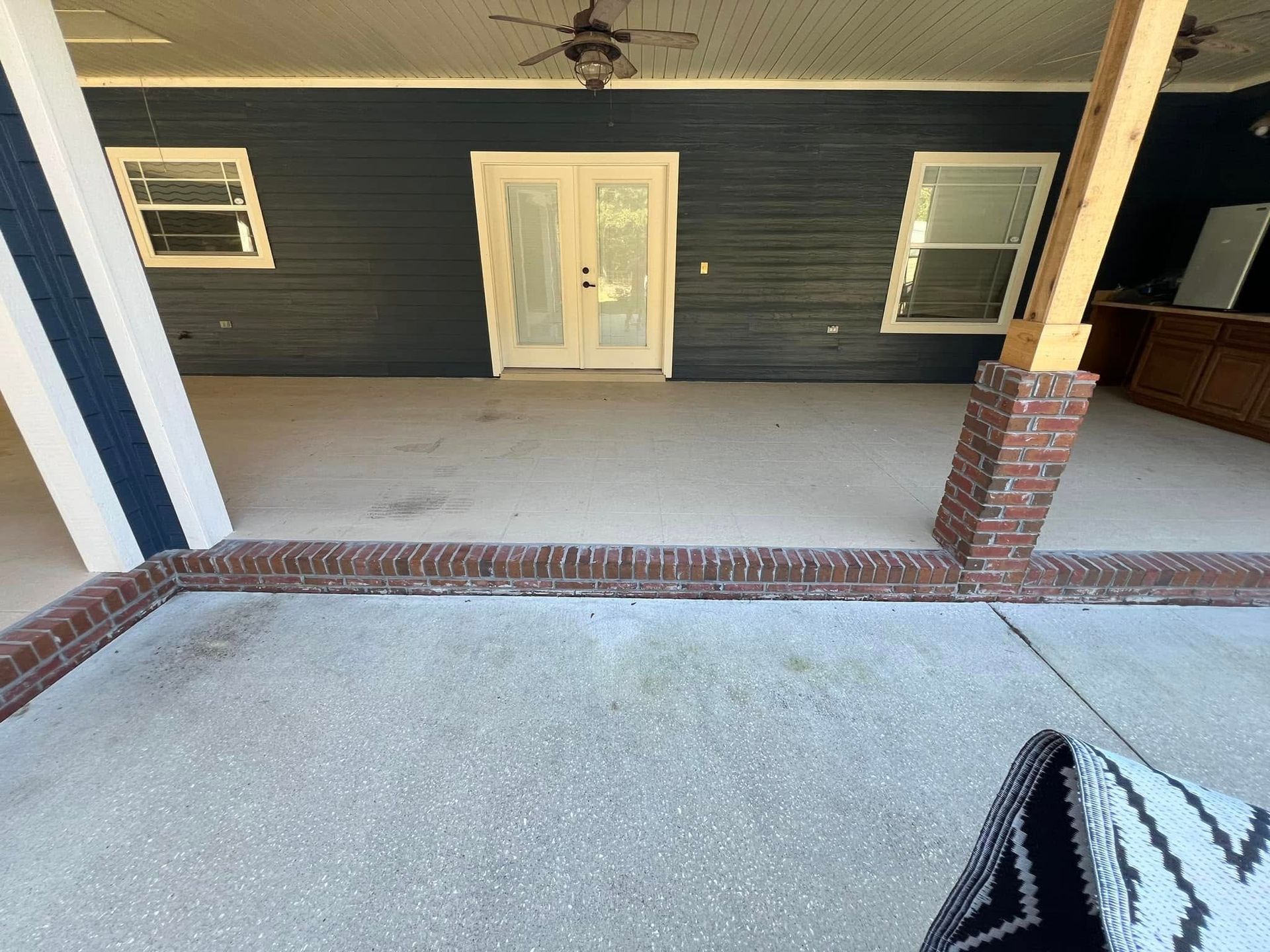 Covered patio with brick trim, blue siding, double doors, and two windows.