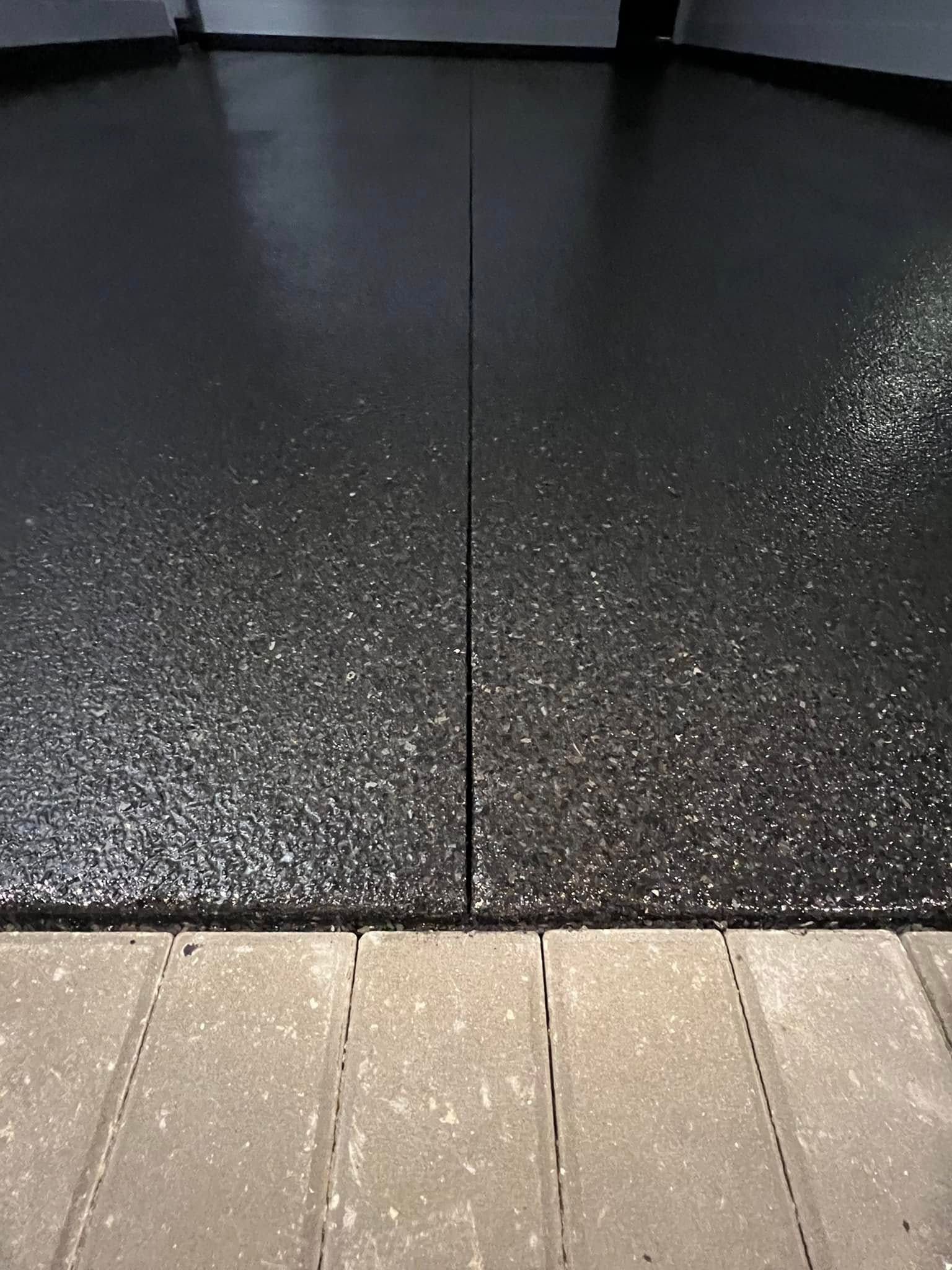 Black speckled epoxy floor with a seam, next to gray brick pavers.
