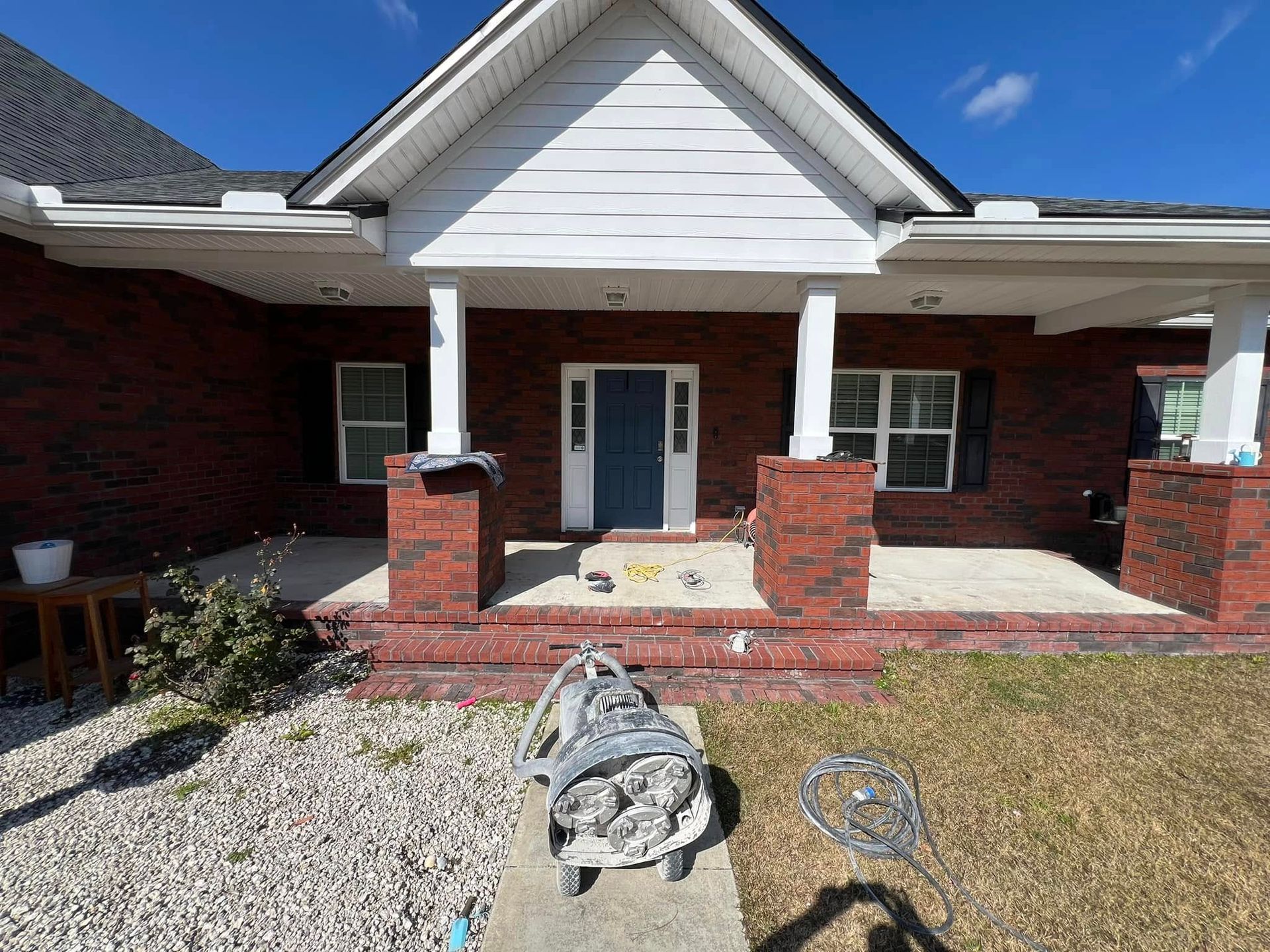 Red brick house with blue door, white trim, and porch, with work materials in front.