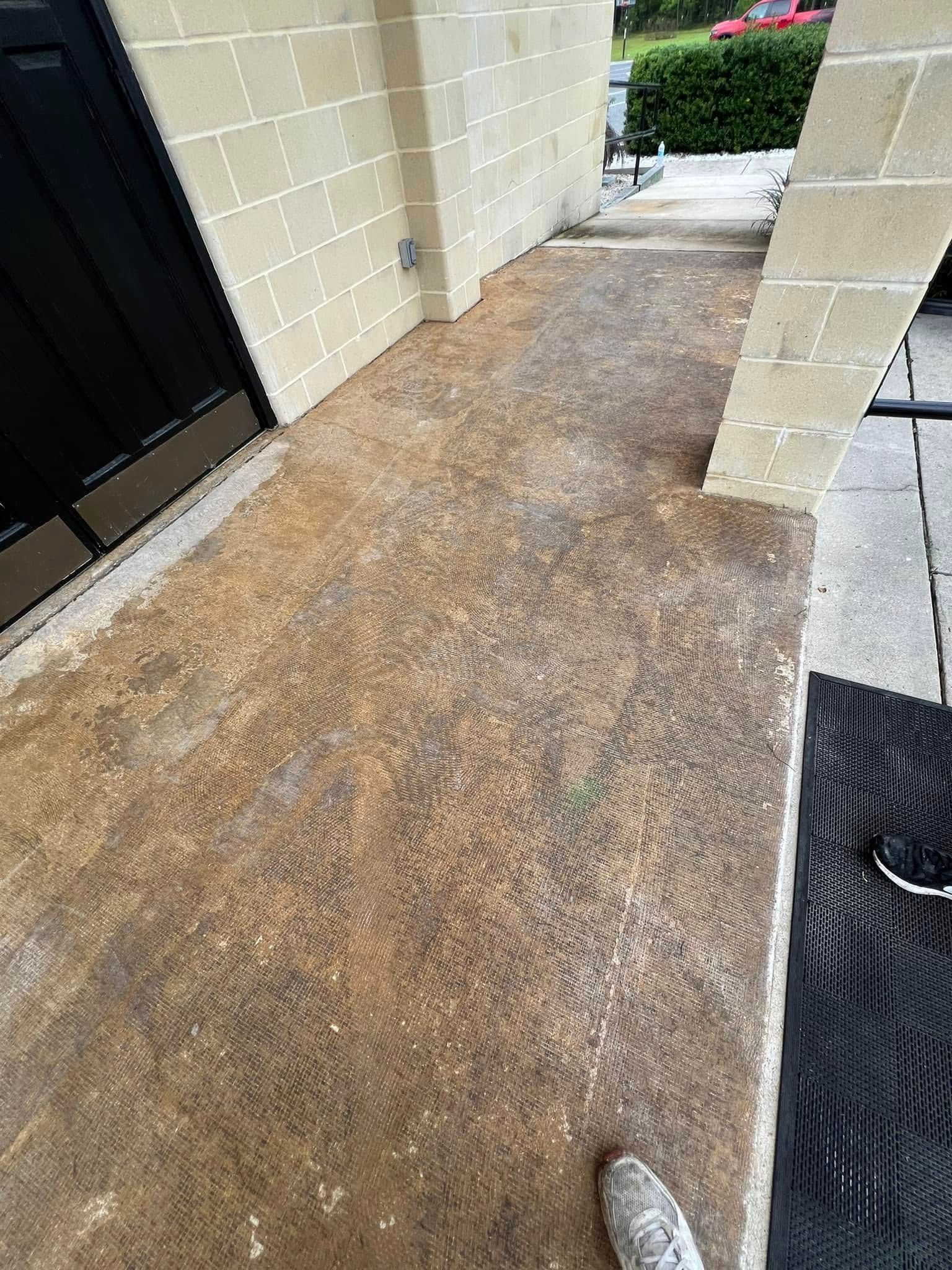 A concrete walkway in front of a building with a black door. Tan block walls.