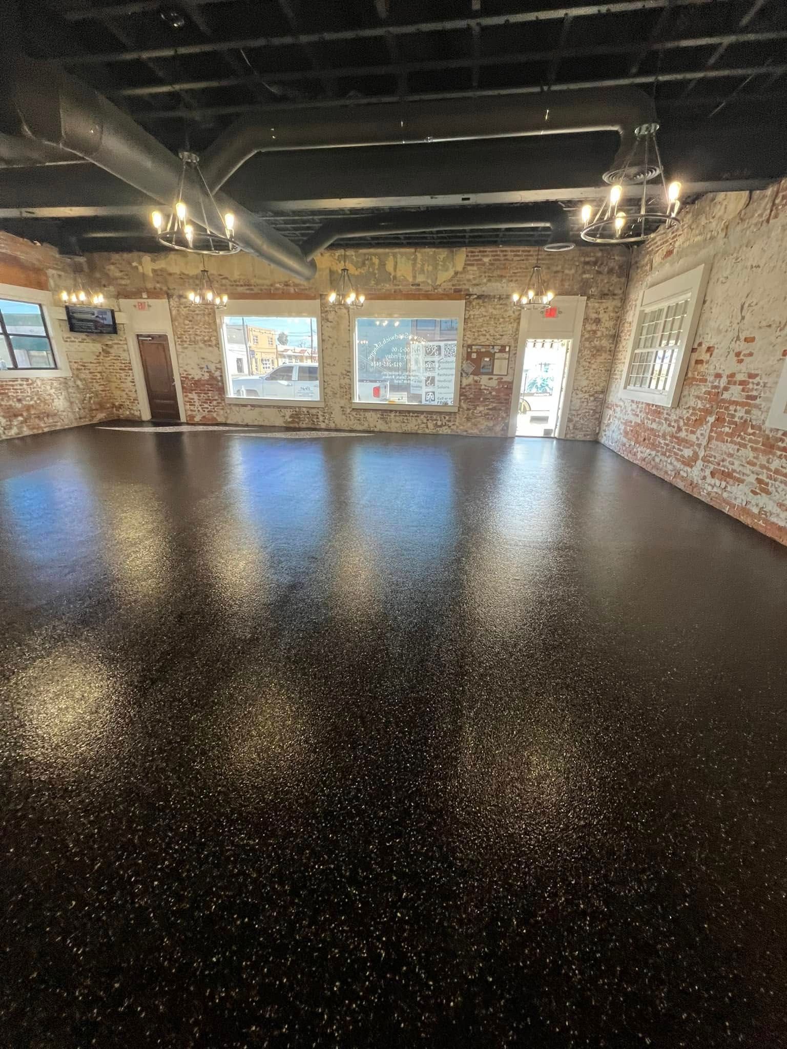 Shiny black floor in a large room with exposed brick walls and windows.