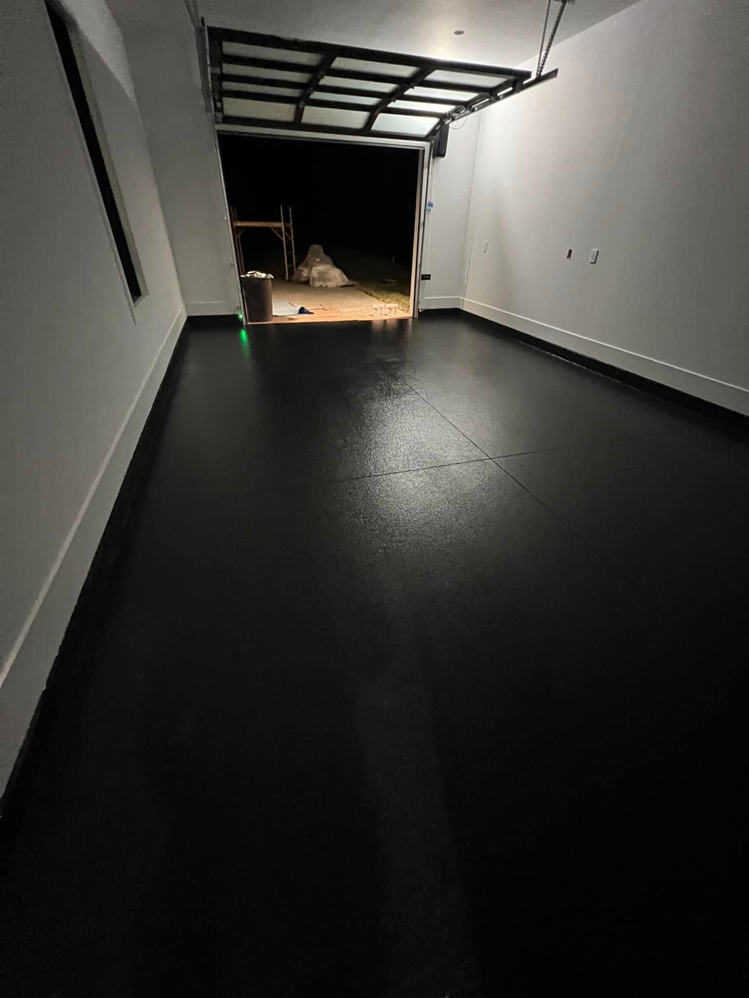 Dark garage interior with black floor, white walls, and open garage door.