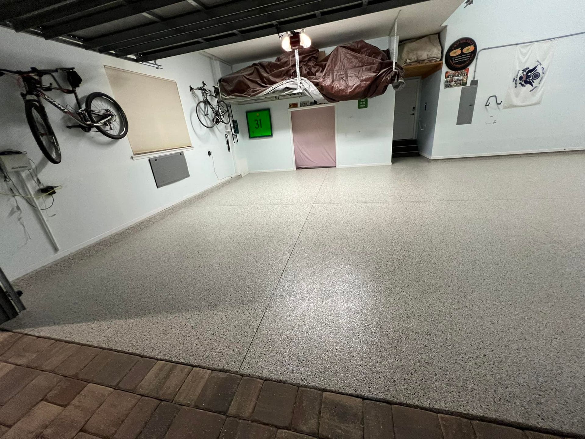Empty garage with speckled floor, bikes on wall, and overhead storage.