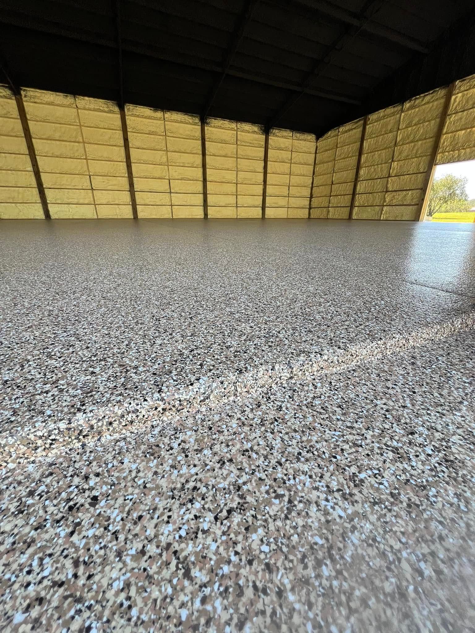 Speckled epoxy floor in a warehouse, with stacked light-colored materials in the background.