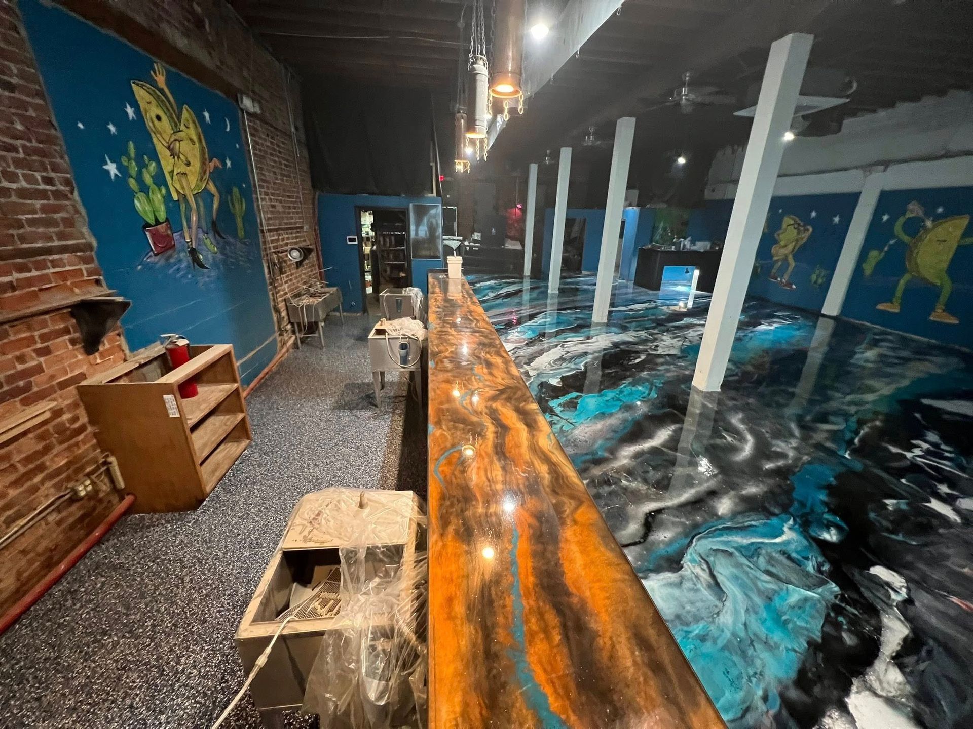 Bar with a colorful epoxy floor and counter. Artwork on walls.