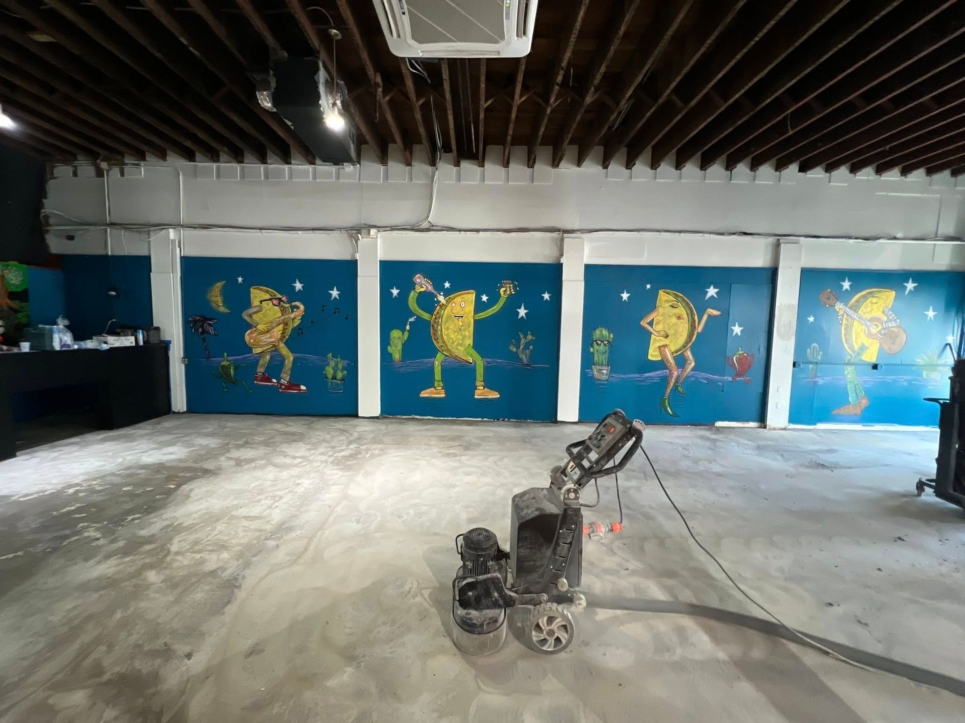 Room with cartoon murals of lemons on blue walls; floor grinder in foreground.