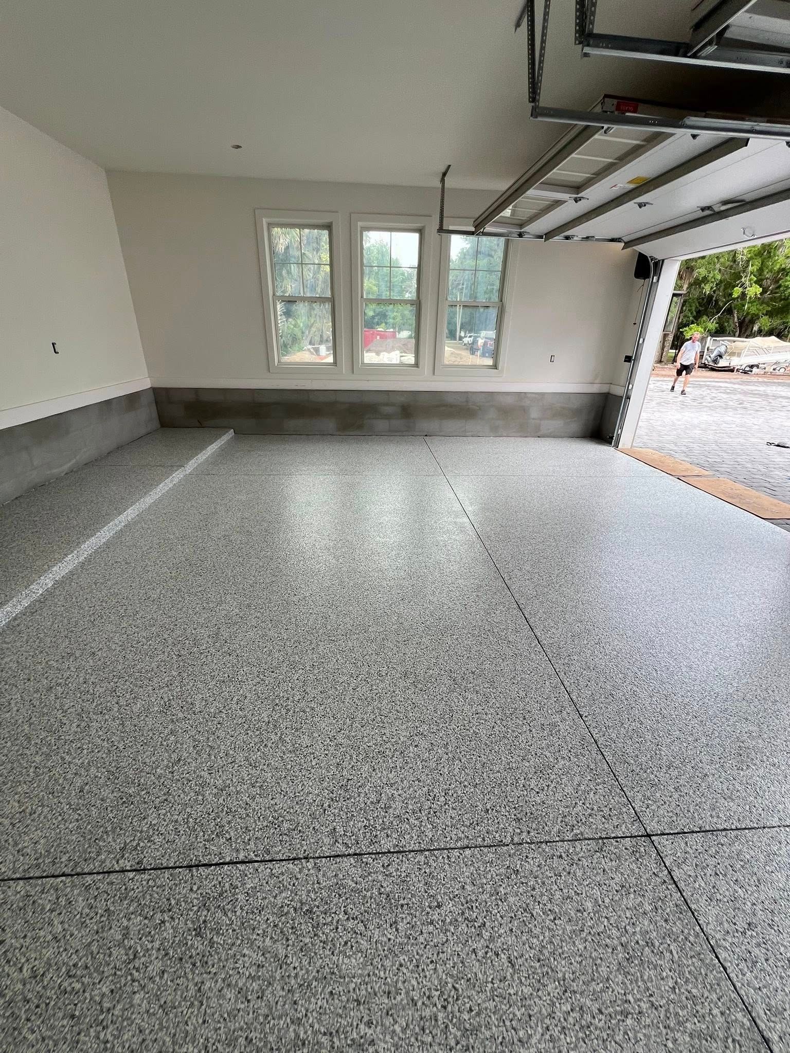 Garage with speckled gray epoxy floor, three windows, and a partially open garage door.