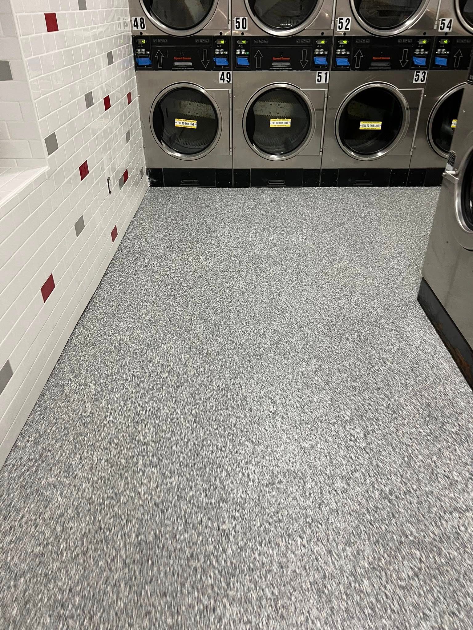 Laundromat interior with washers, a gray speckled floor, and a stack of white boxes with red and gray accents.