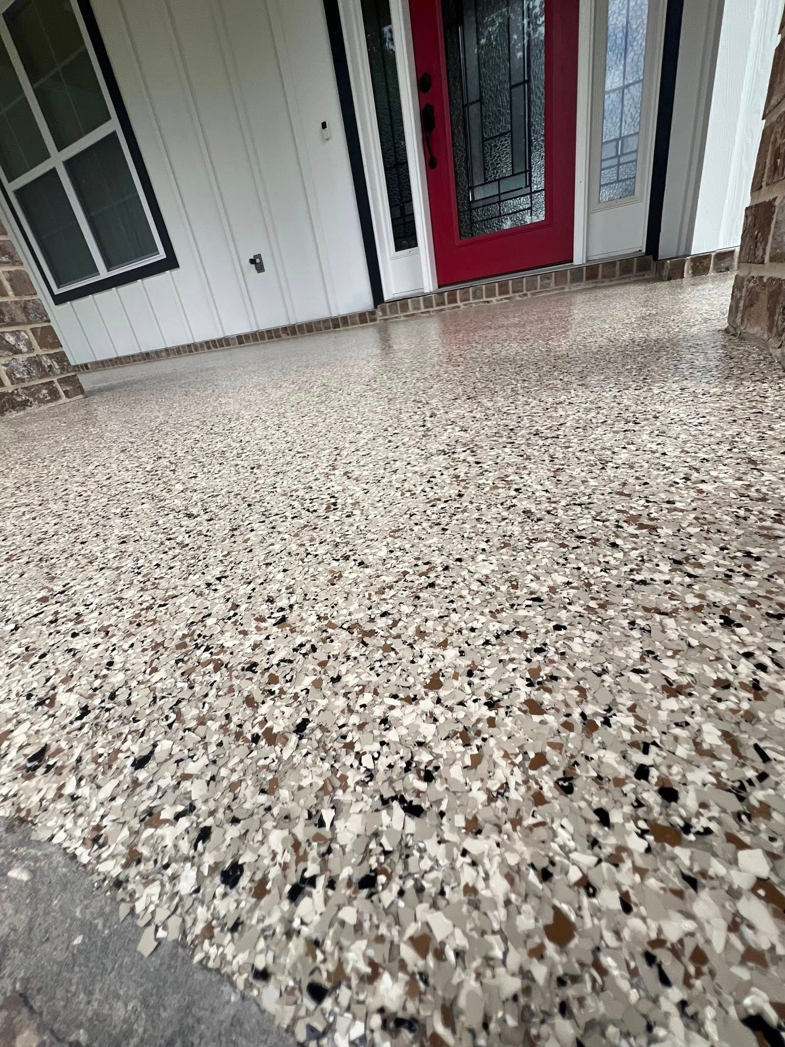 Close-up view of a porch floor covered in a speckled epoxy coating. The door is red.