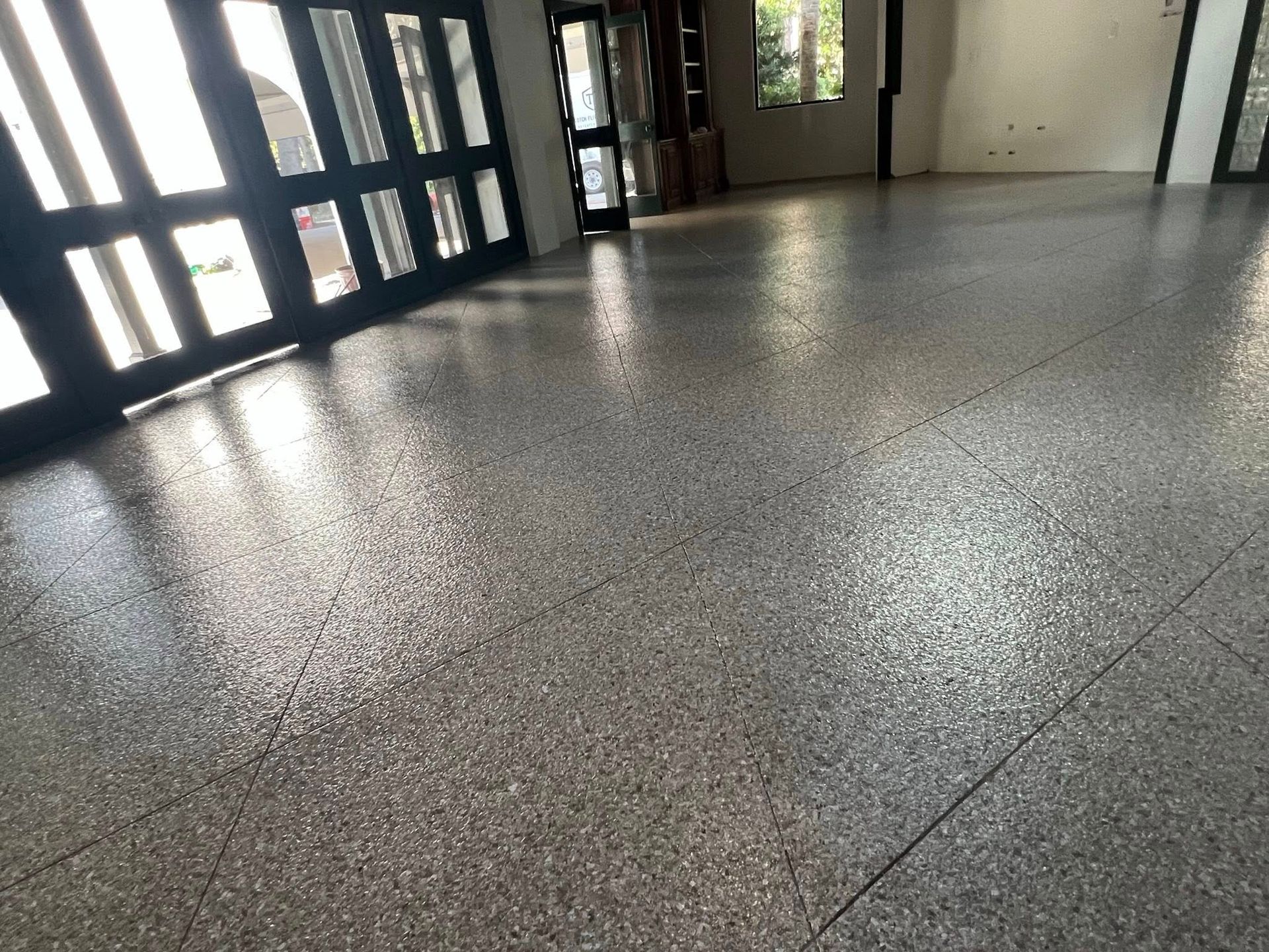 Gray epoxy floor with speckled details, reflecting sunlight from a garage door and windows.