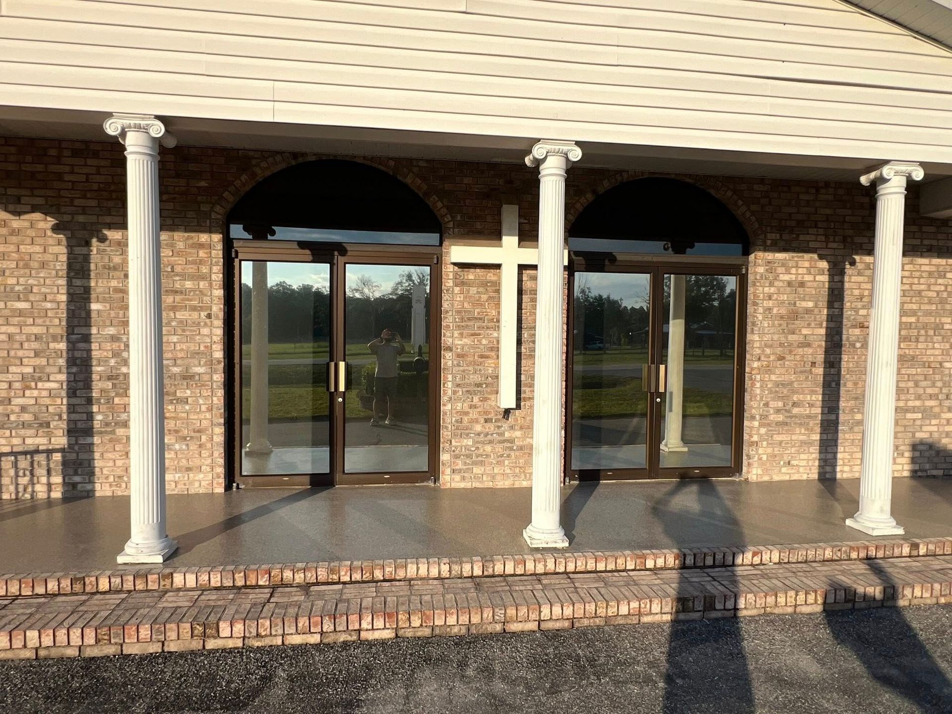 Church entrance with columns, brick, and glass doors; a cross is visible.