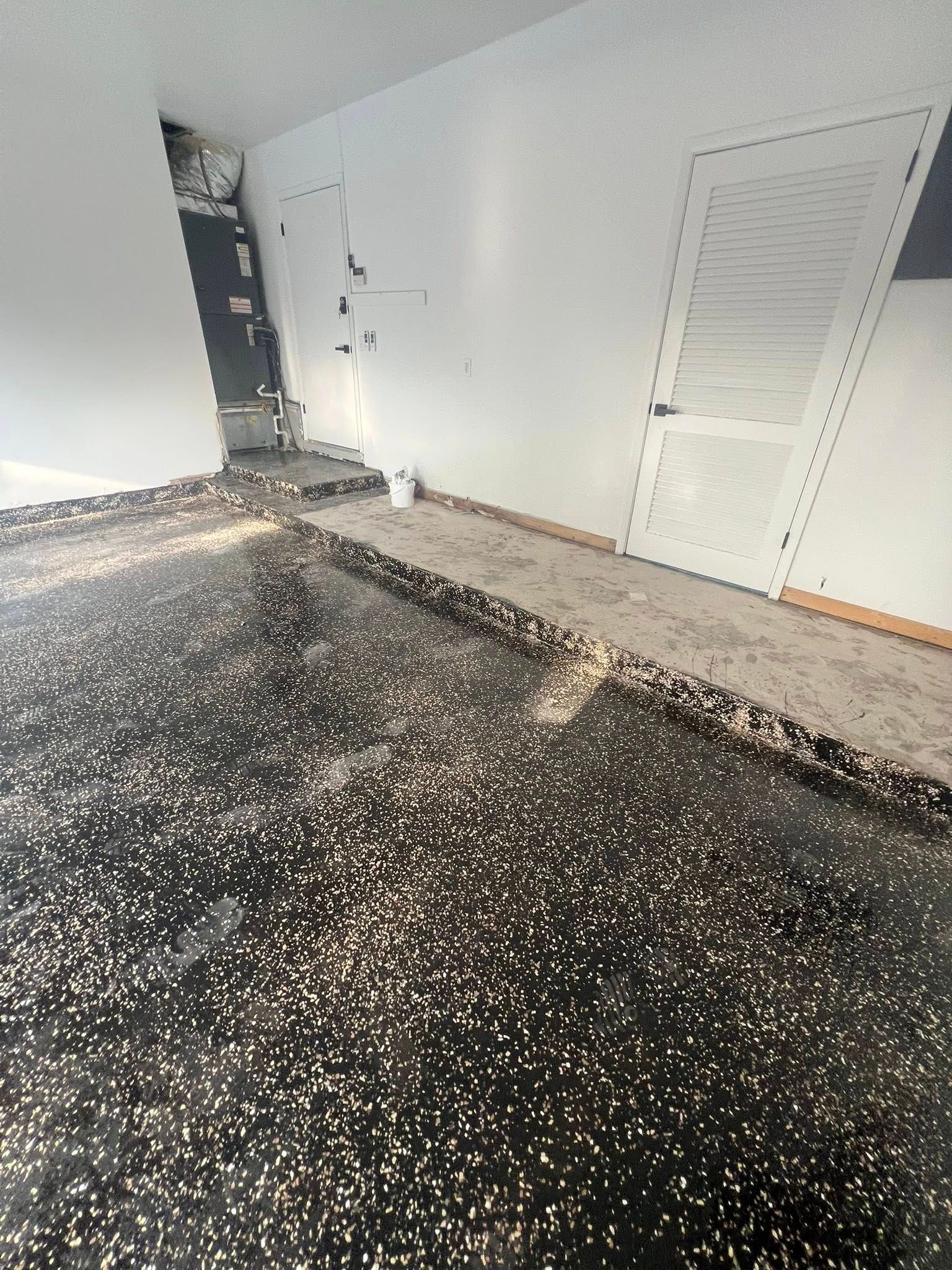 Room with speckled black flooring. White walls, two doors, a bucket.