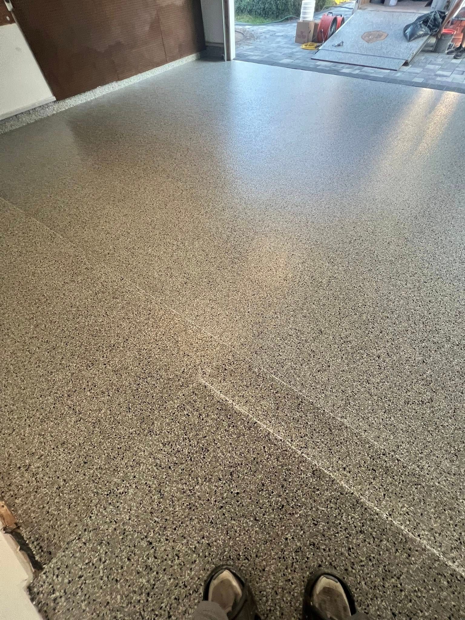 Garage floor with speckled epoxy coating. Dark and light flecks on a shiny surface.