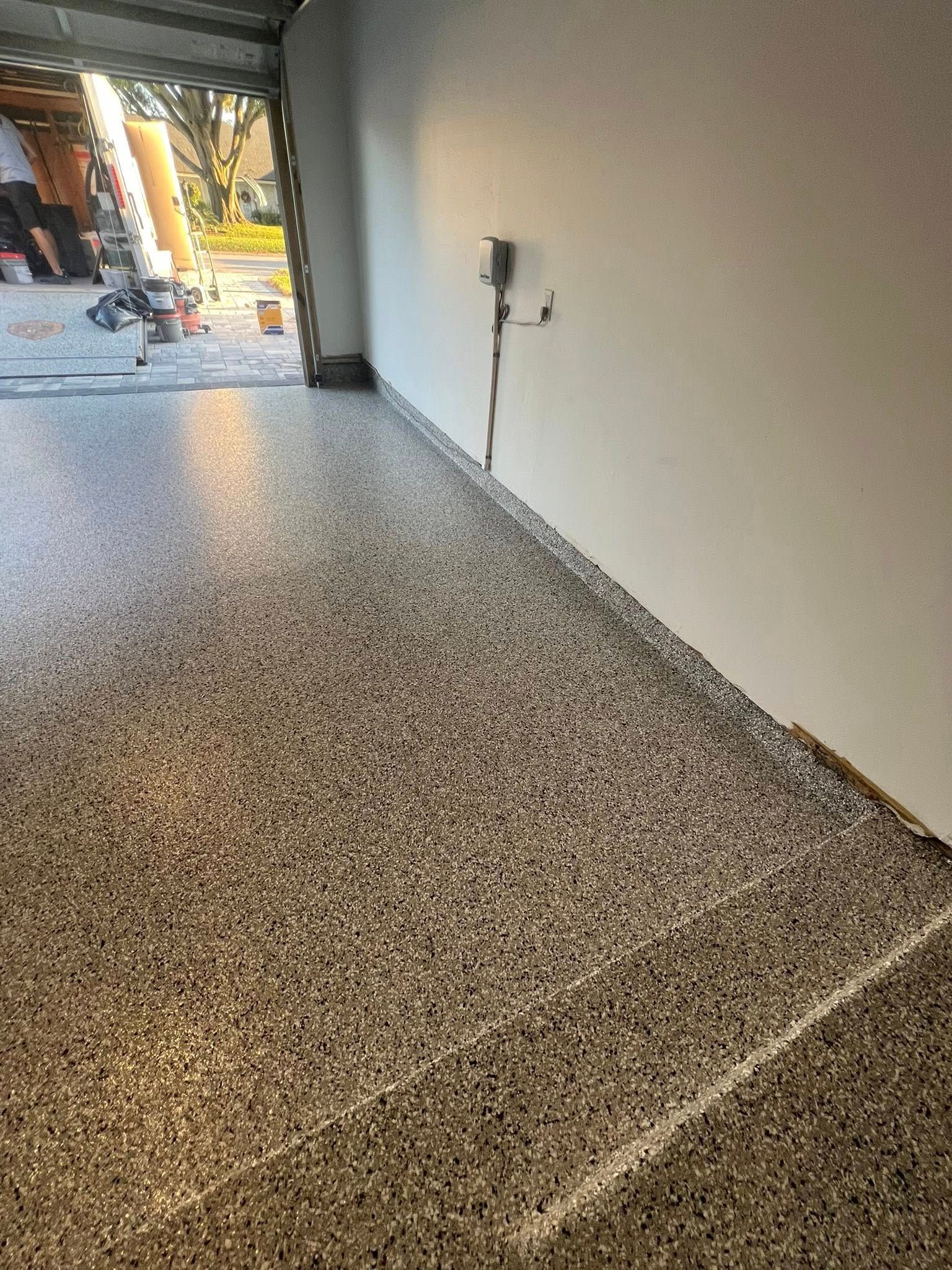 Epoxy-coated garage floor with speckled gray and white aggregate. A power outlet is visible on a white wall.