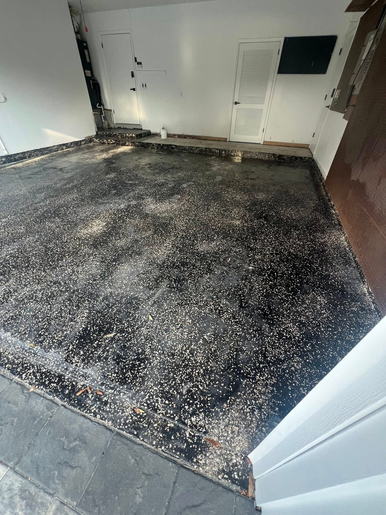 Dark, speckled flooring with flaking paint in a room with white walls and a ceiling vent.