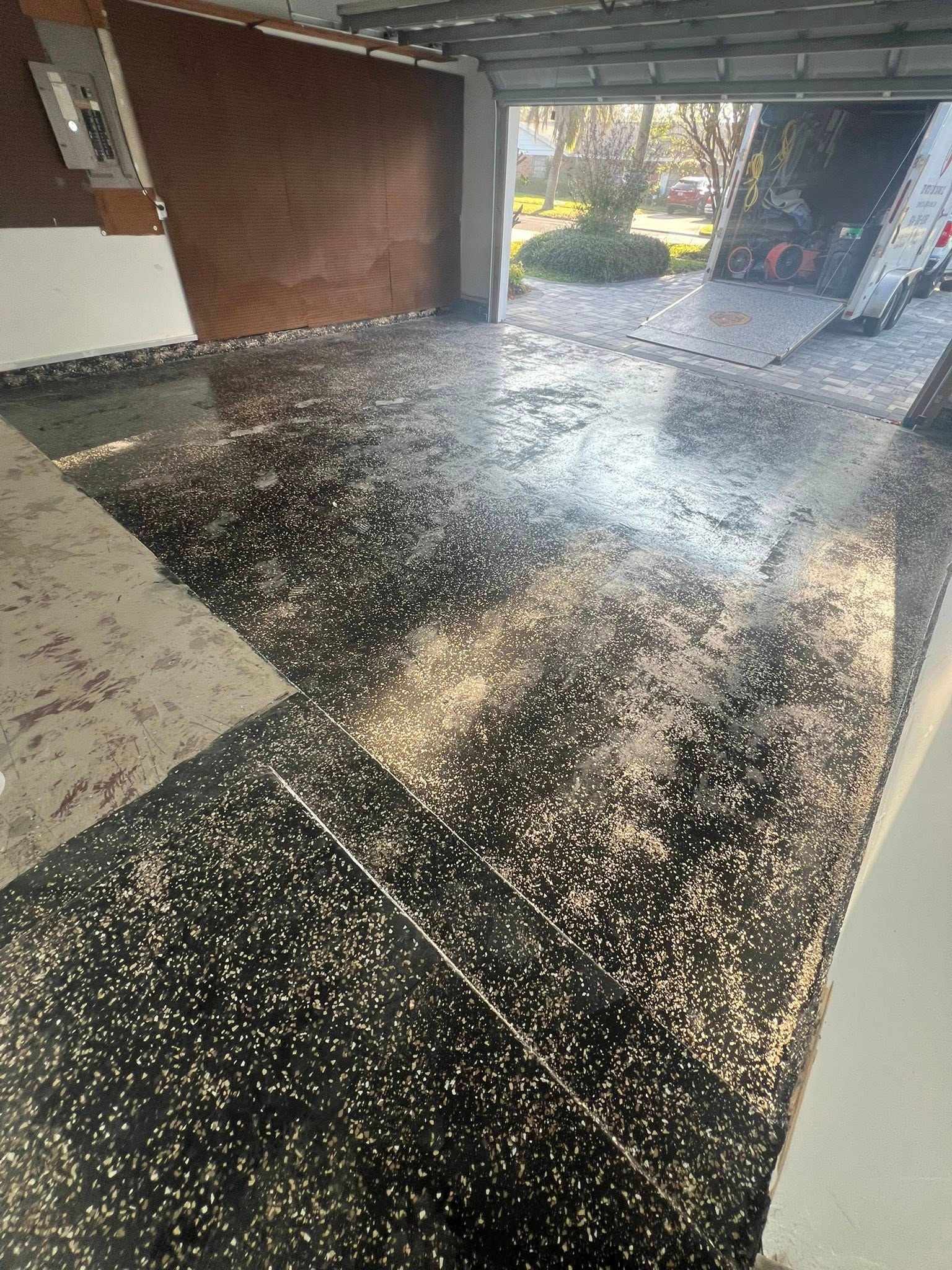 Garage floor with black and white speckled coating, opening to driveway and sunlight.