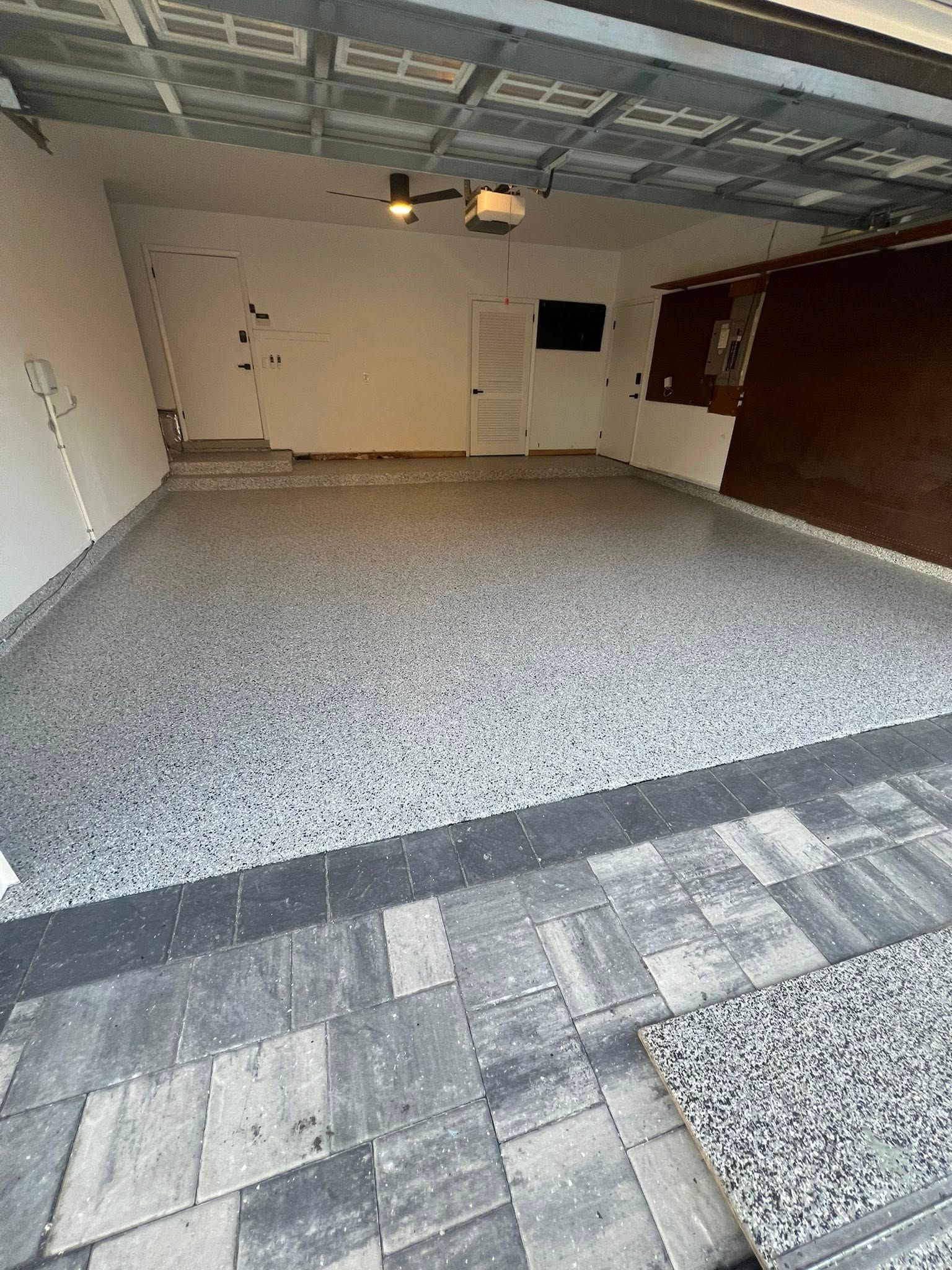 Garage interior with speckled gray floor and dark gray and light gray pavers outside.