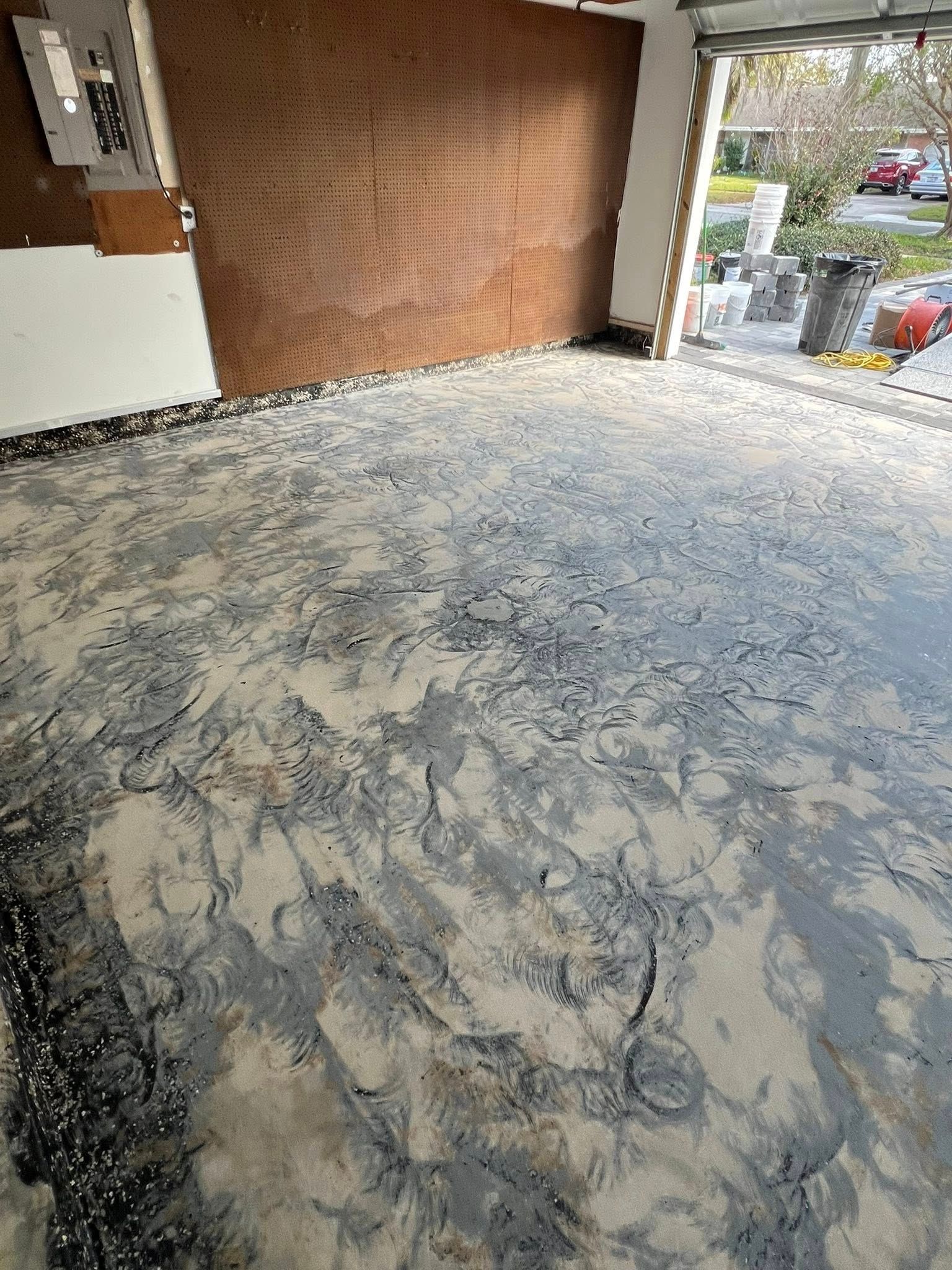Garage floor with a textured, mottled gray and tan epoxy coating; wood-paneled wall.